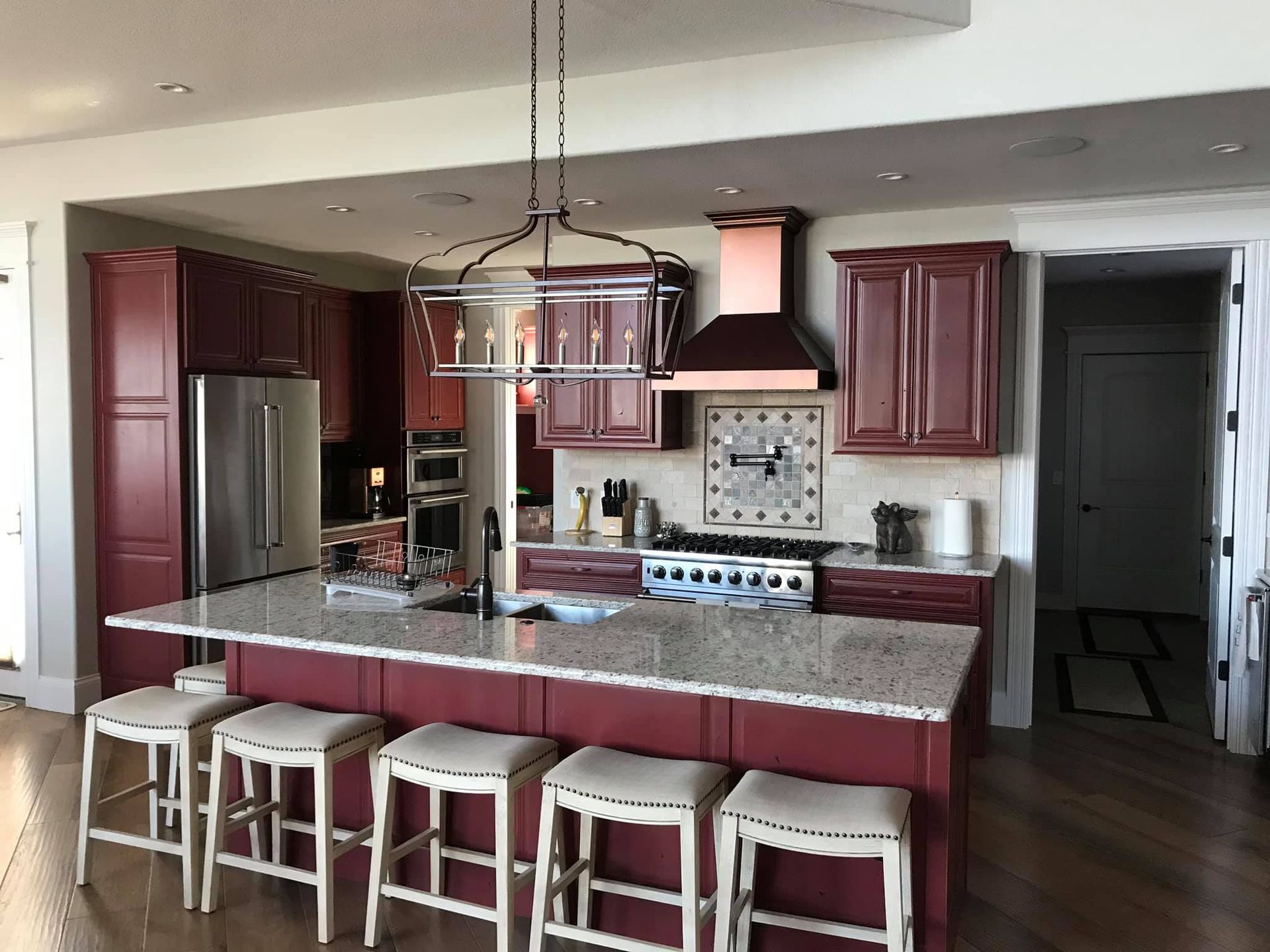Modern kitchen with burgundy cabinets, stainless fridge, granite island, and four stools