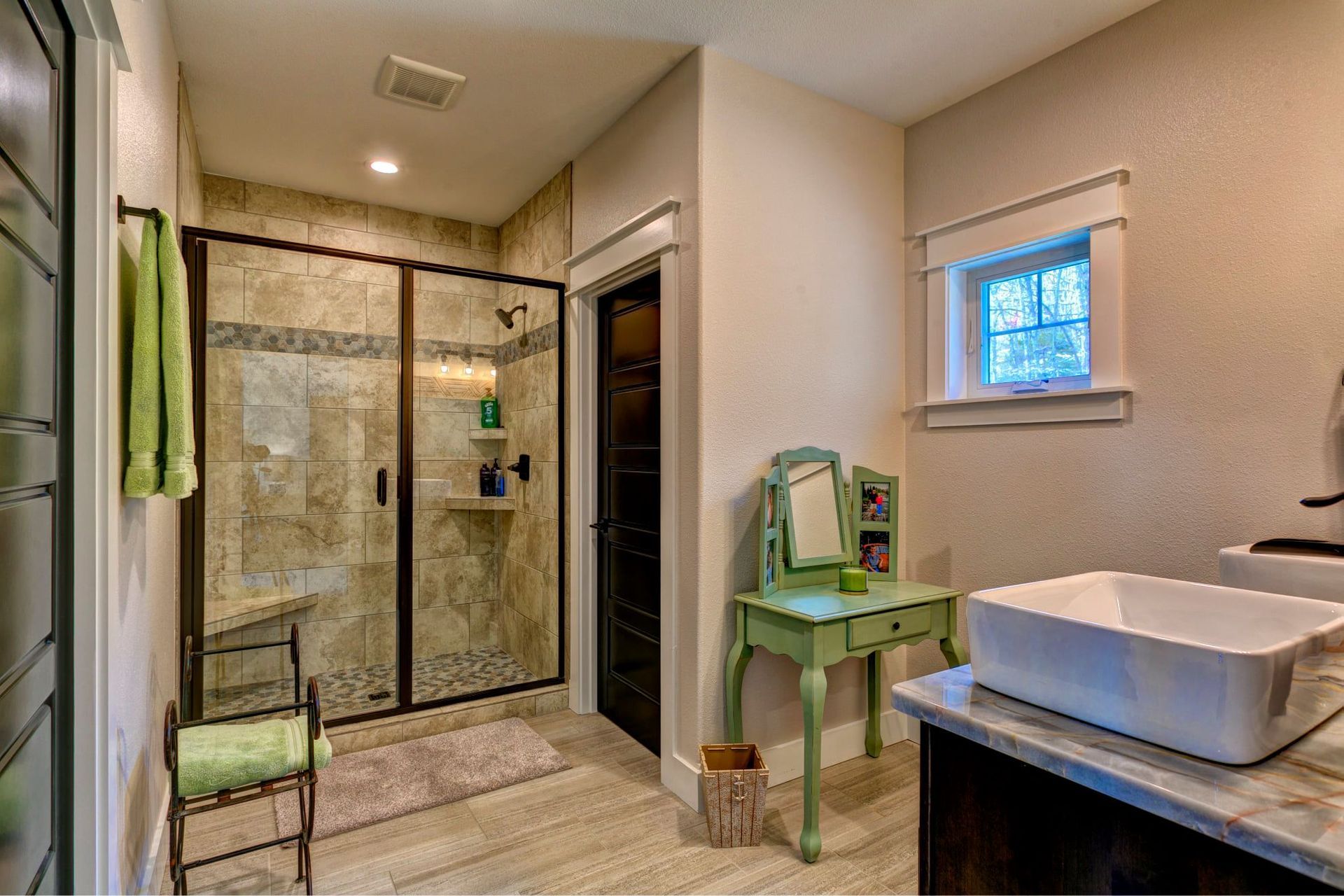 Modern bathroom with glass shower, green vanity, sink, and small window