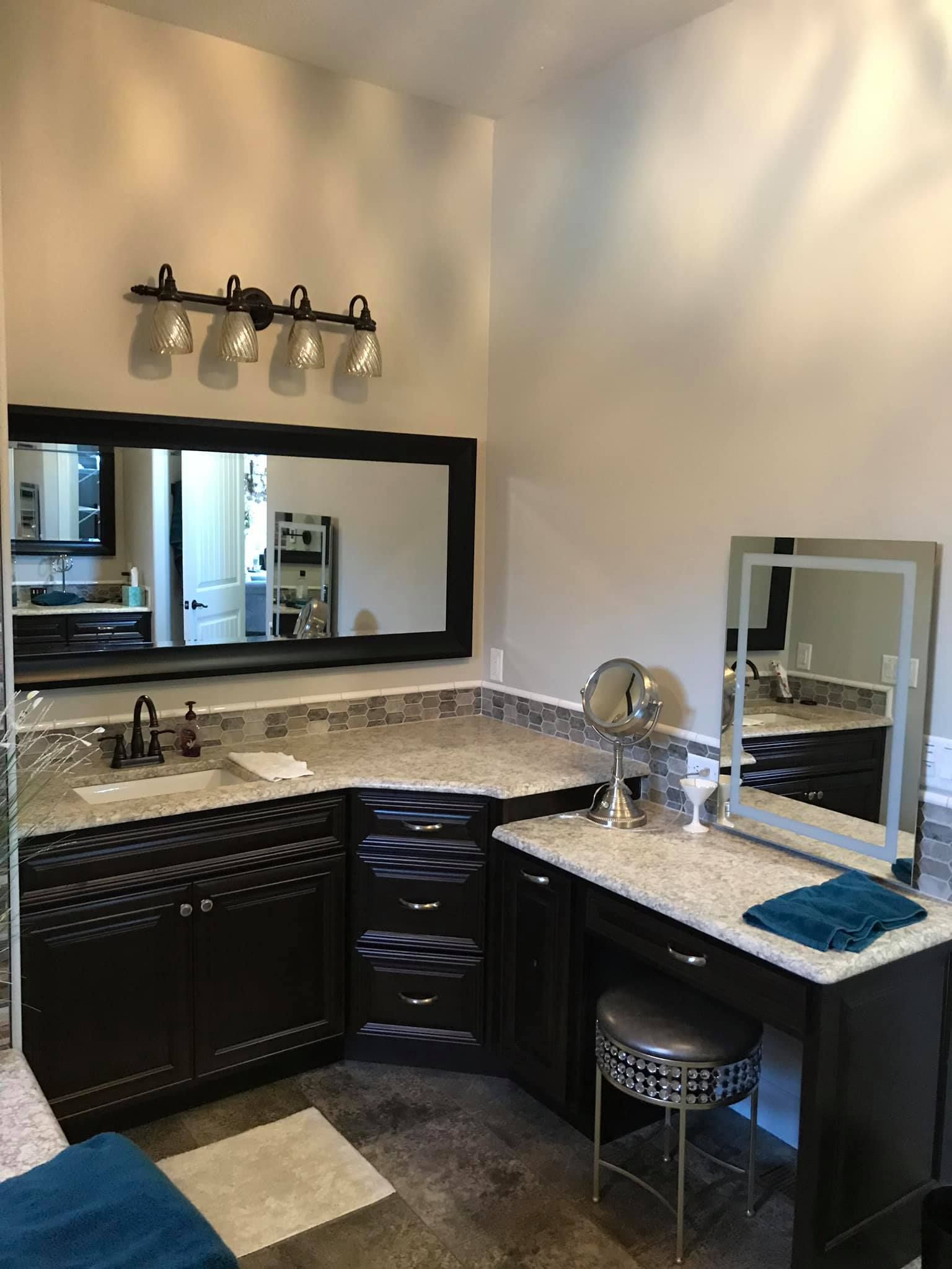 Modern bathroom vanity with black cabinets, granite countertop, mirror, wall lights, and makeup station