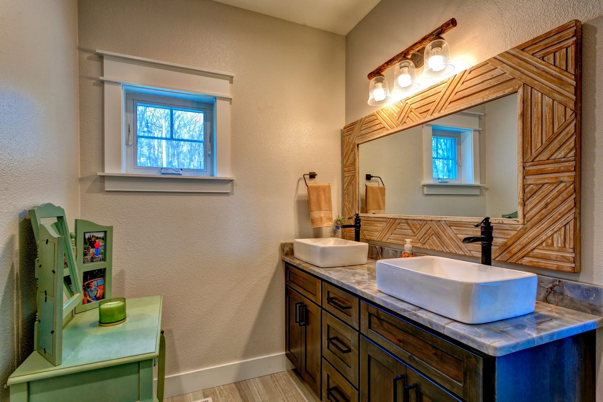 Small bathroom with double vanity, wood-framed mirror, and mint-green toilet near a window.