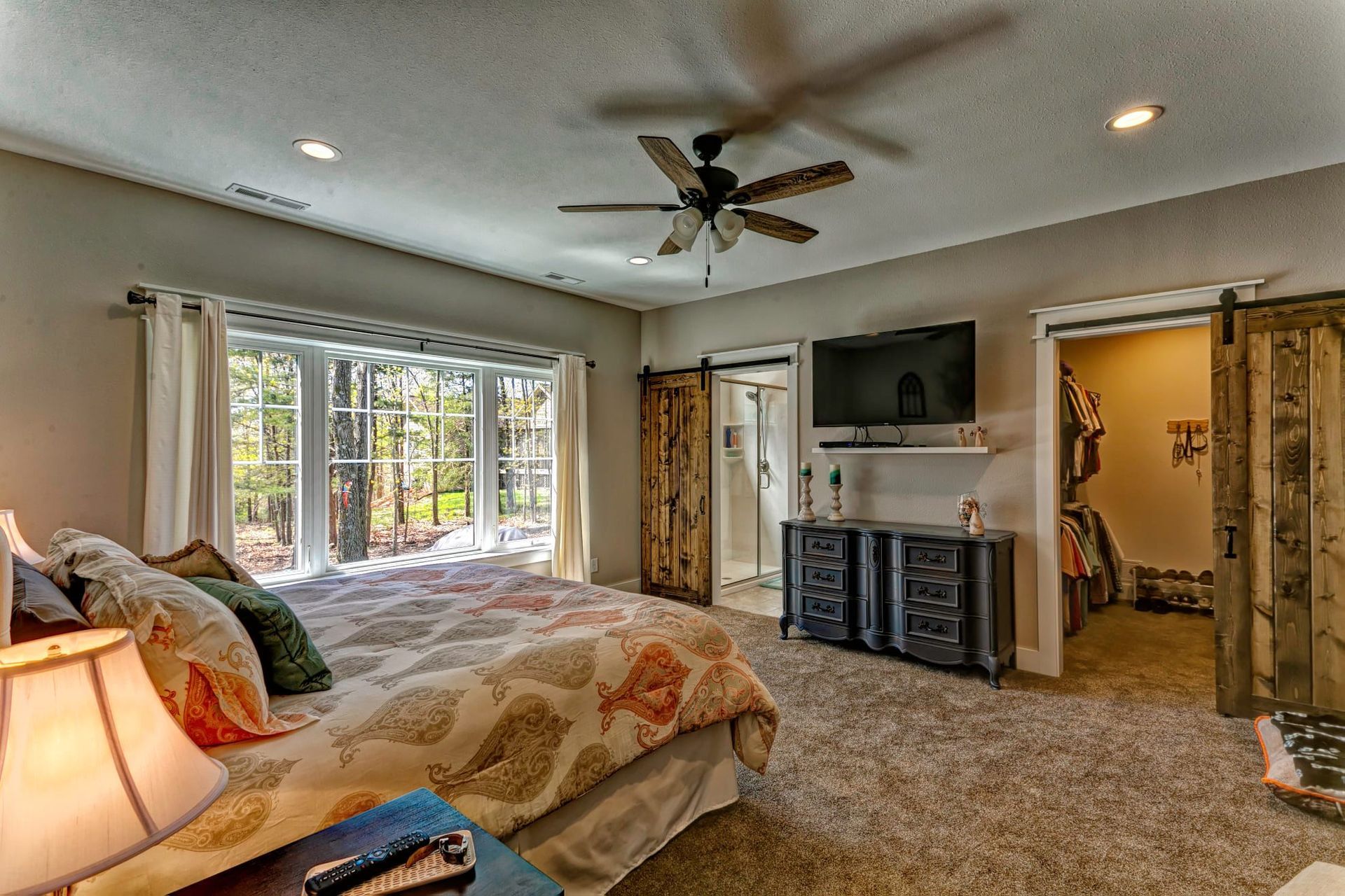Spacious bedroom with a large bed, TV above a fireplace, and window seat overlooking trees