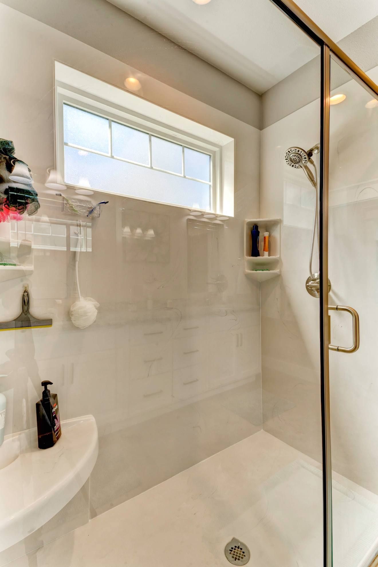 Bright white bathroom shower with glass door, window, and wall-mounted shelves.