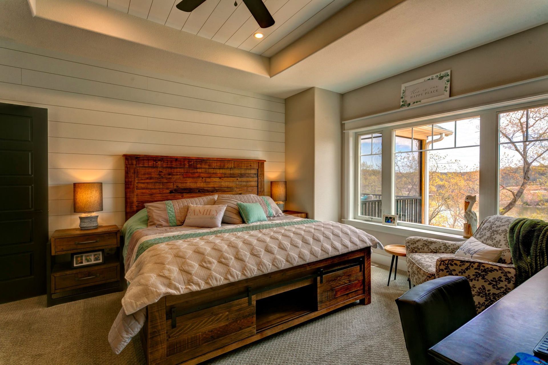 Cozy bedroom with wood bed, bedside lamp, large windows, and seating area overlooking trees
