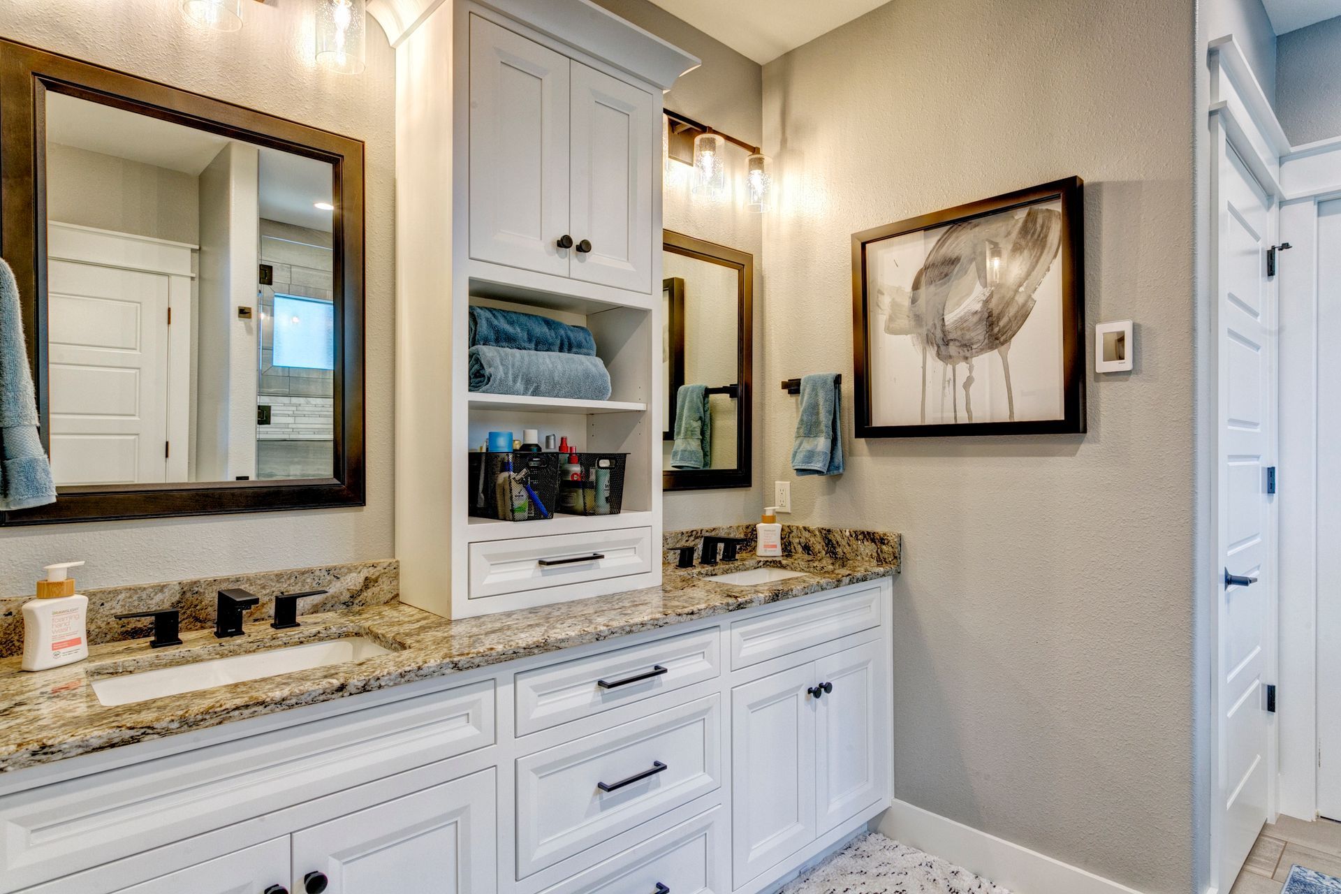 Elegant bathroom vanity with granite countertop, double mirrors, and white cabinetry under warm lighting