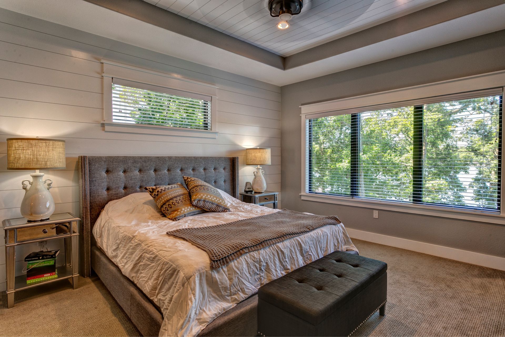 Bright bedroom with tufted bed, beige decor, and large windows overlooking trees