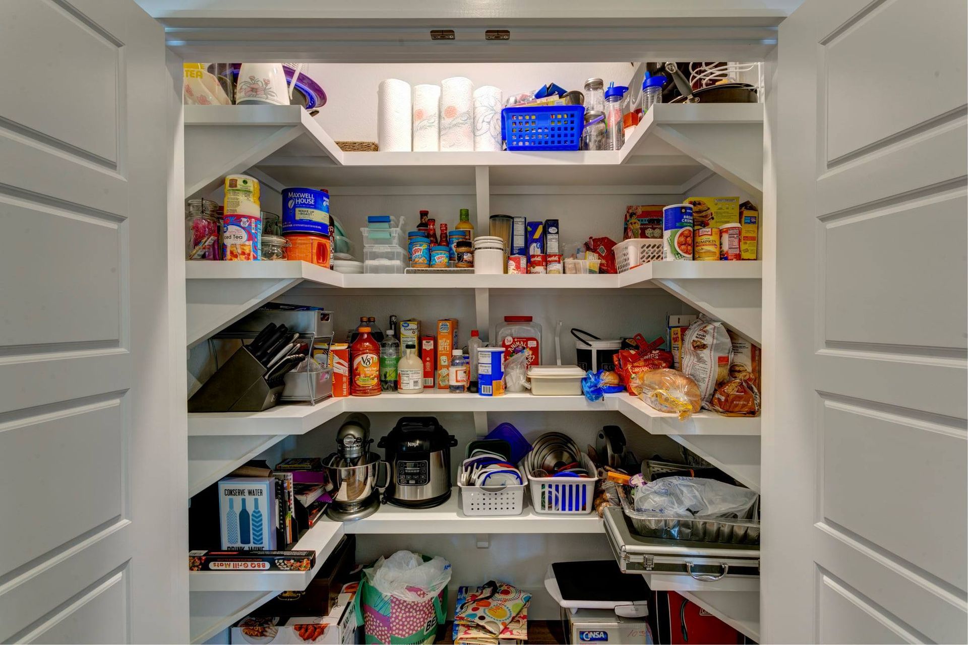 Open pantry filled with assorted snacks, canned goods, and kitchen supplies on white shelves.