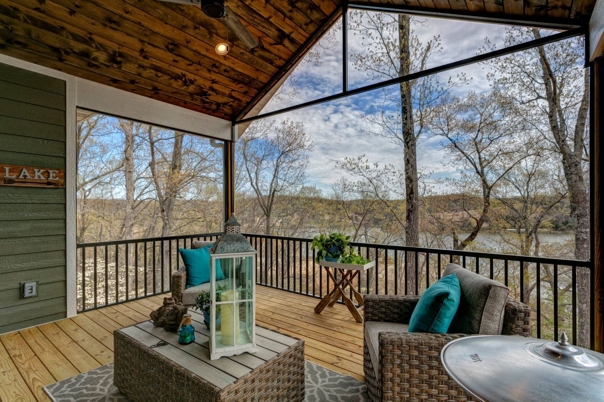 Covered porch with wicker seating, turquoise cushions, and a wooded view through railings.
