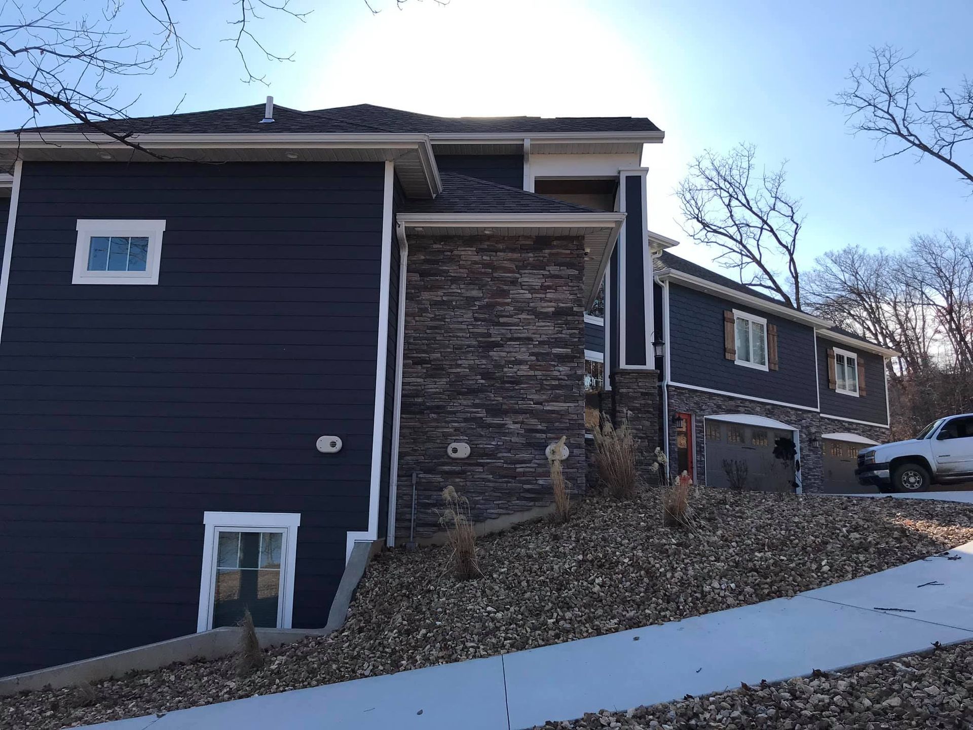 Dark blue house with stone chimney on a sloped hillside, seen from the street.
