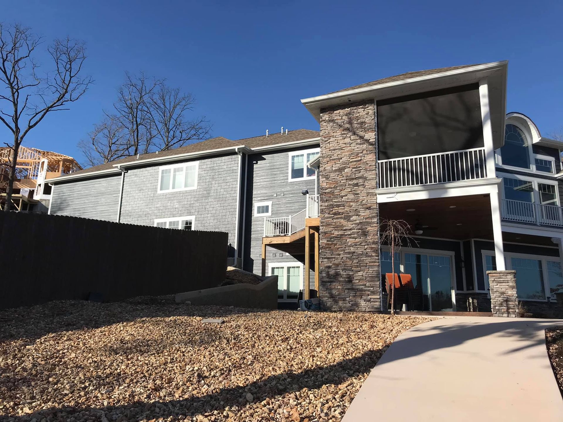 Apartment building exterior with stone balcony, blue sky, and gravel courtyard