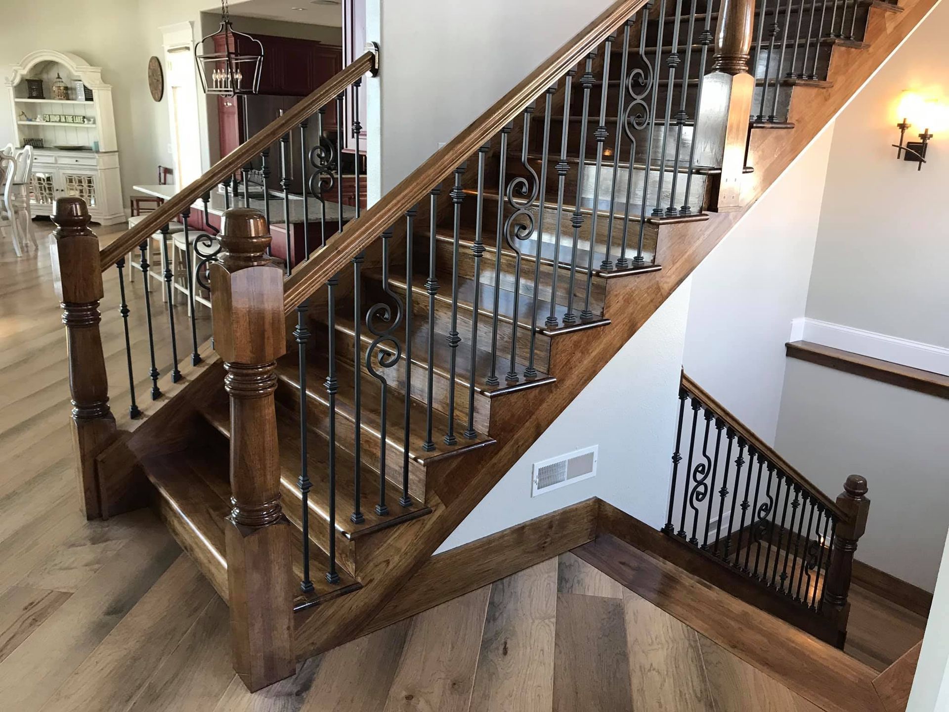 Wooden staircase with dark railing in a beige interior, leading to an upper floor and a basement stairs below