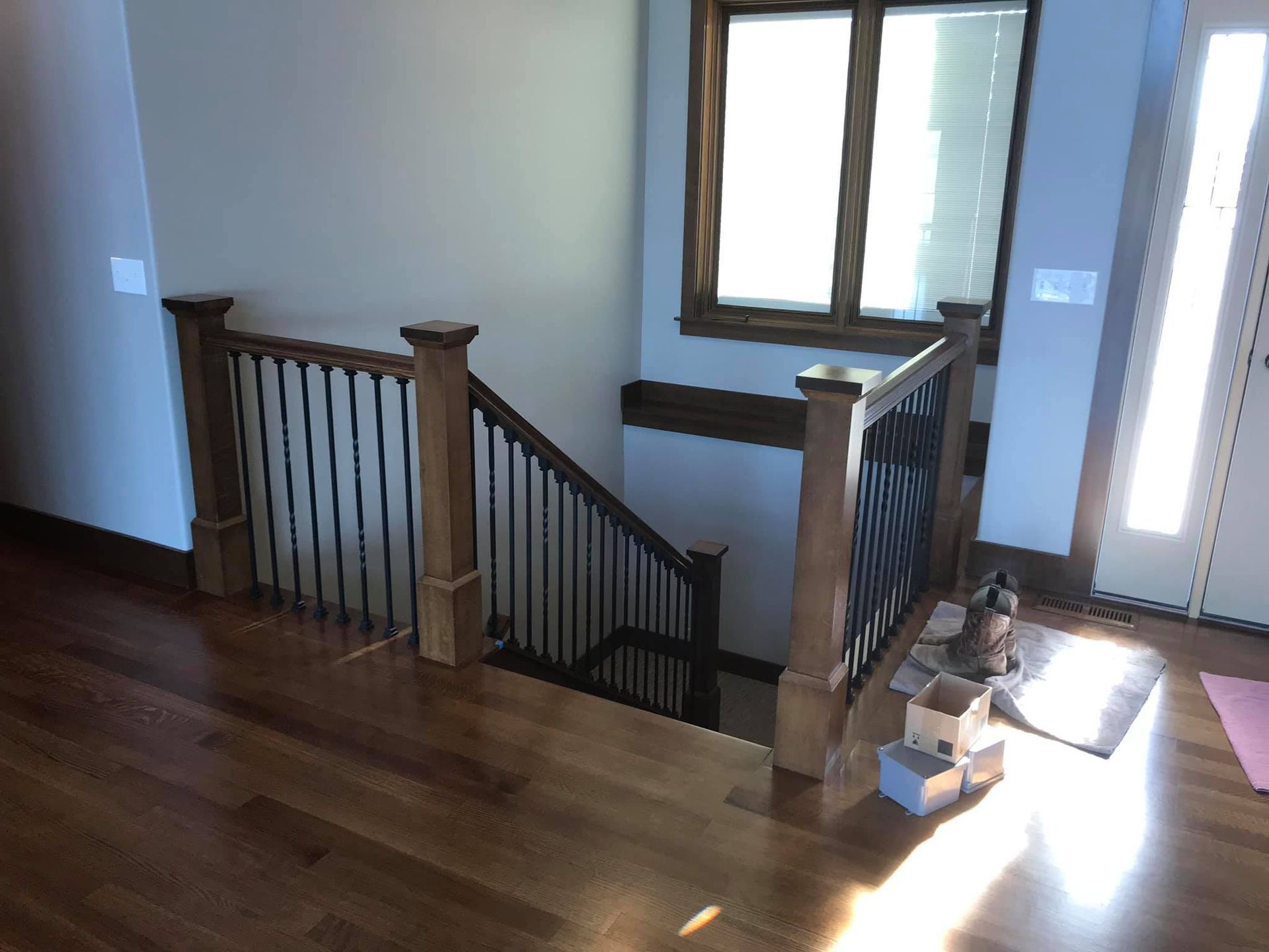 Staircase landing with wooden railing, window, and sunlight on hardwood floor