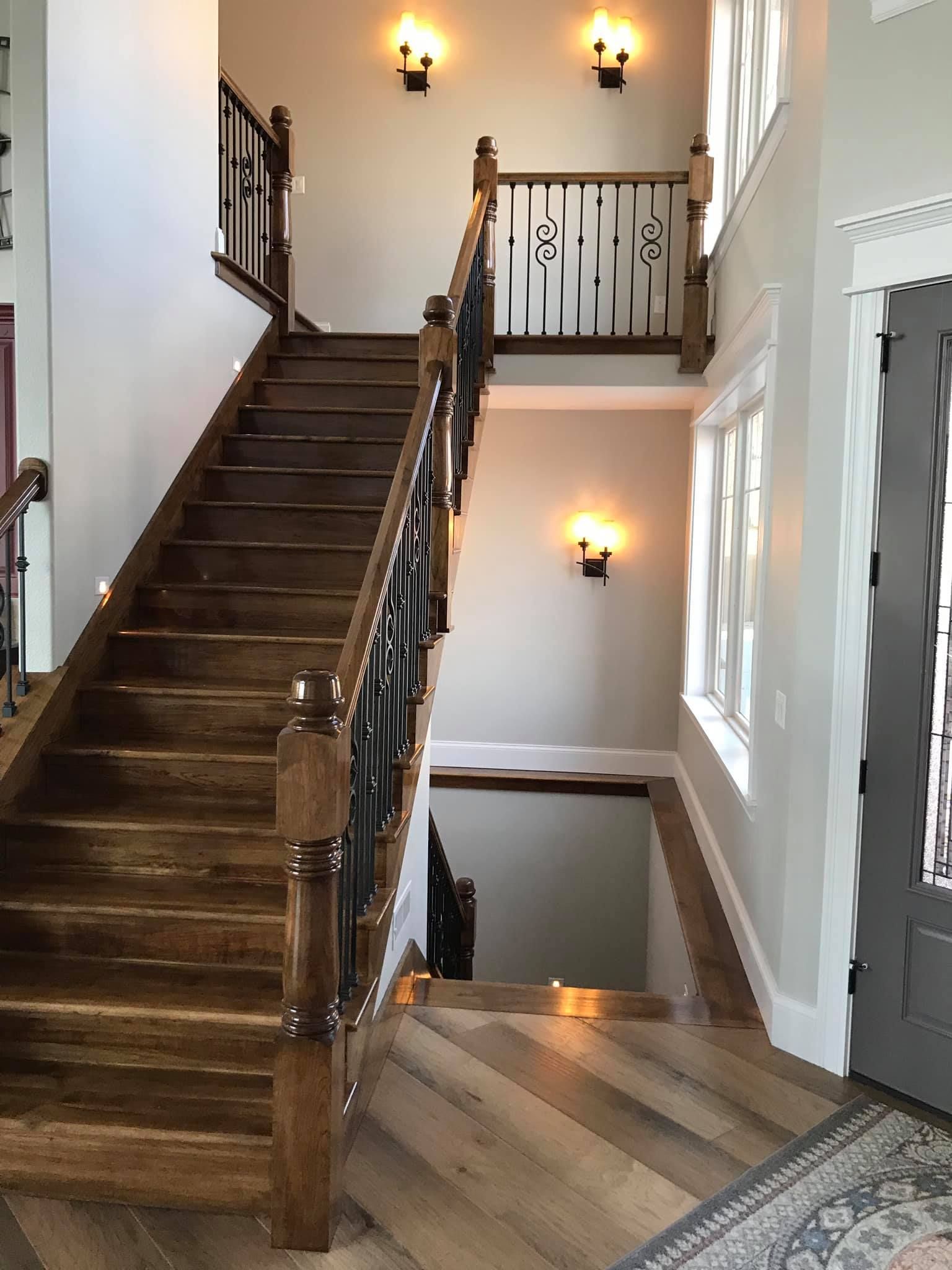 Interior staircase with dark wood railing, white walls, wall sconces, and a carpeted landing.