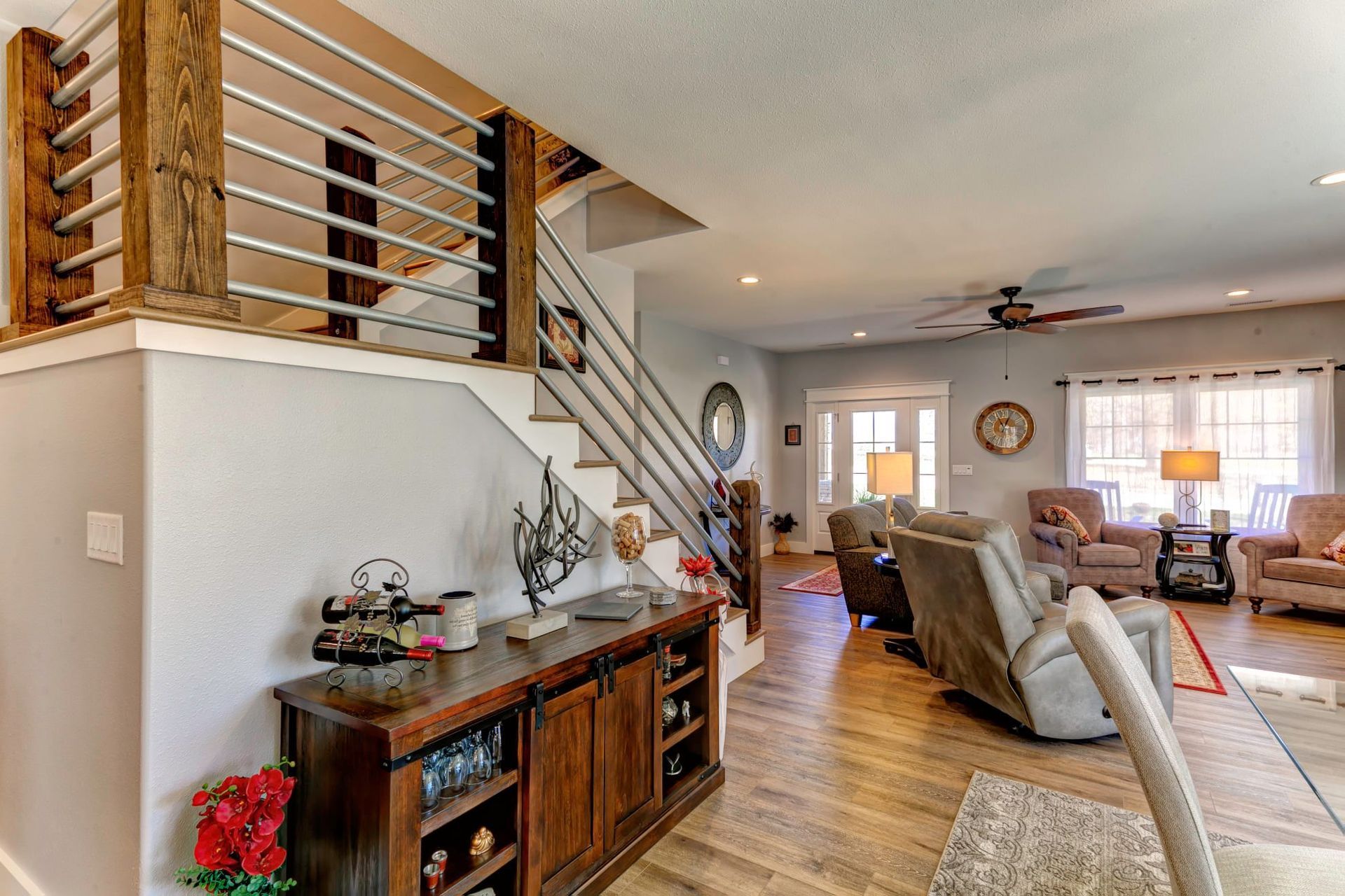 Modern open-plan living room with staircase, leather chairs, hardwood floors, and bright windows