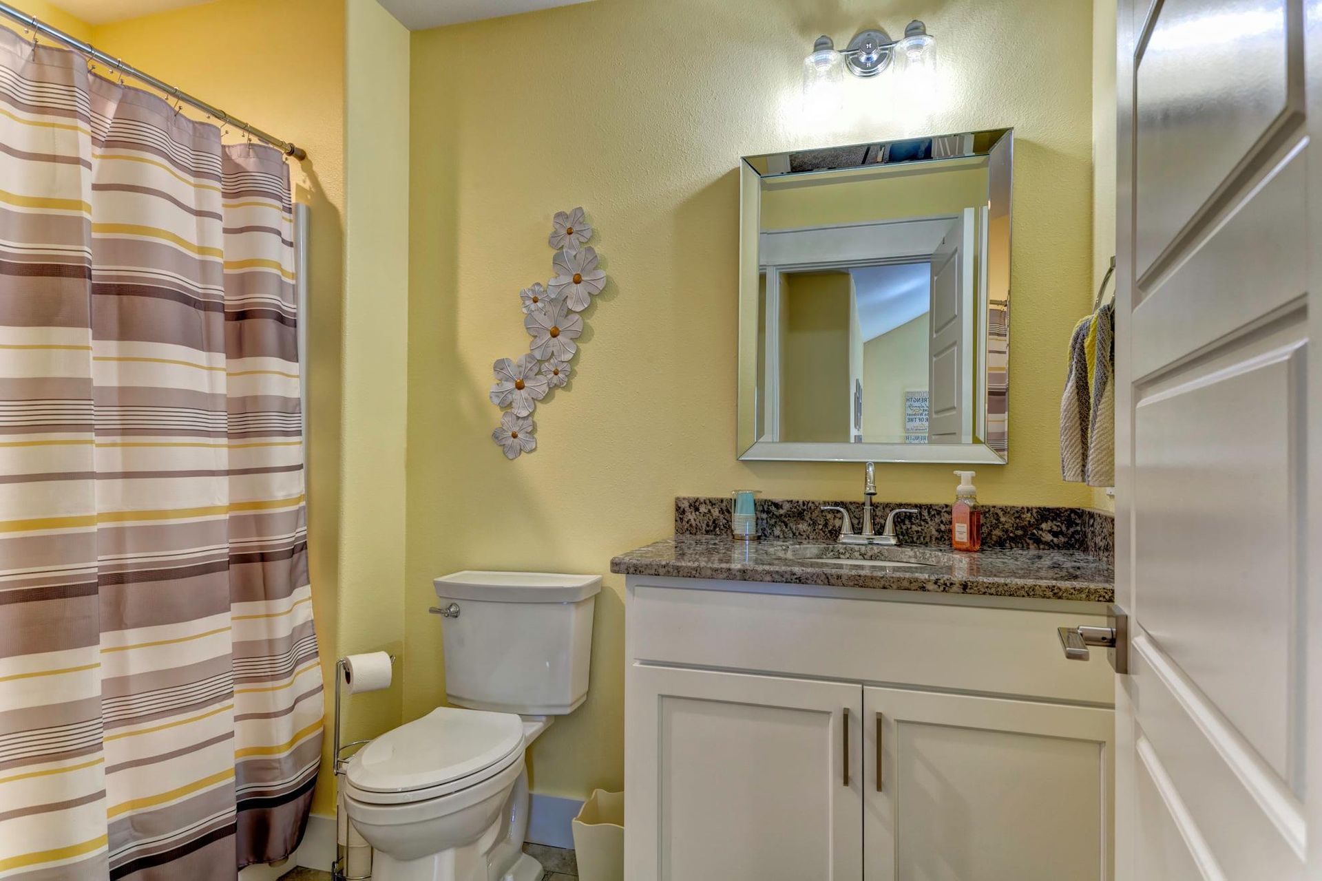 Small bathroom with yellow walls, white vanity, mirror, toilet, and striped shower curtain