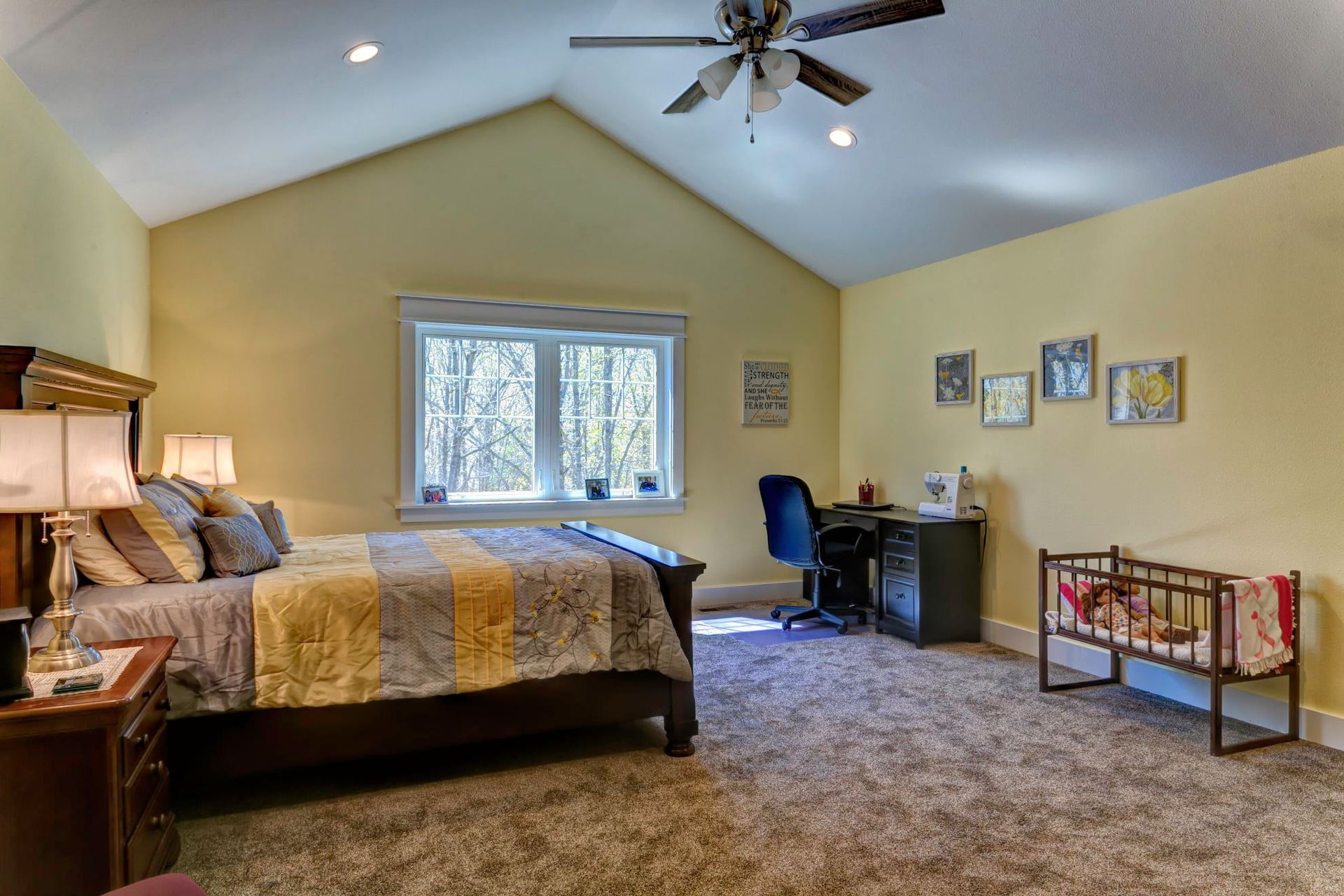 Spacious bedroom with a bed, desk, window, and ceiling fan under a vaulted ceiling.