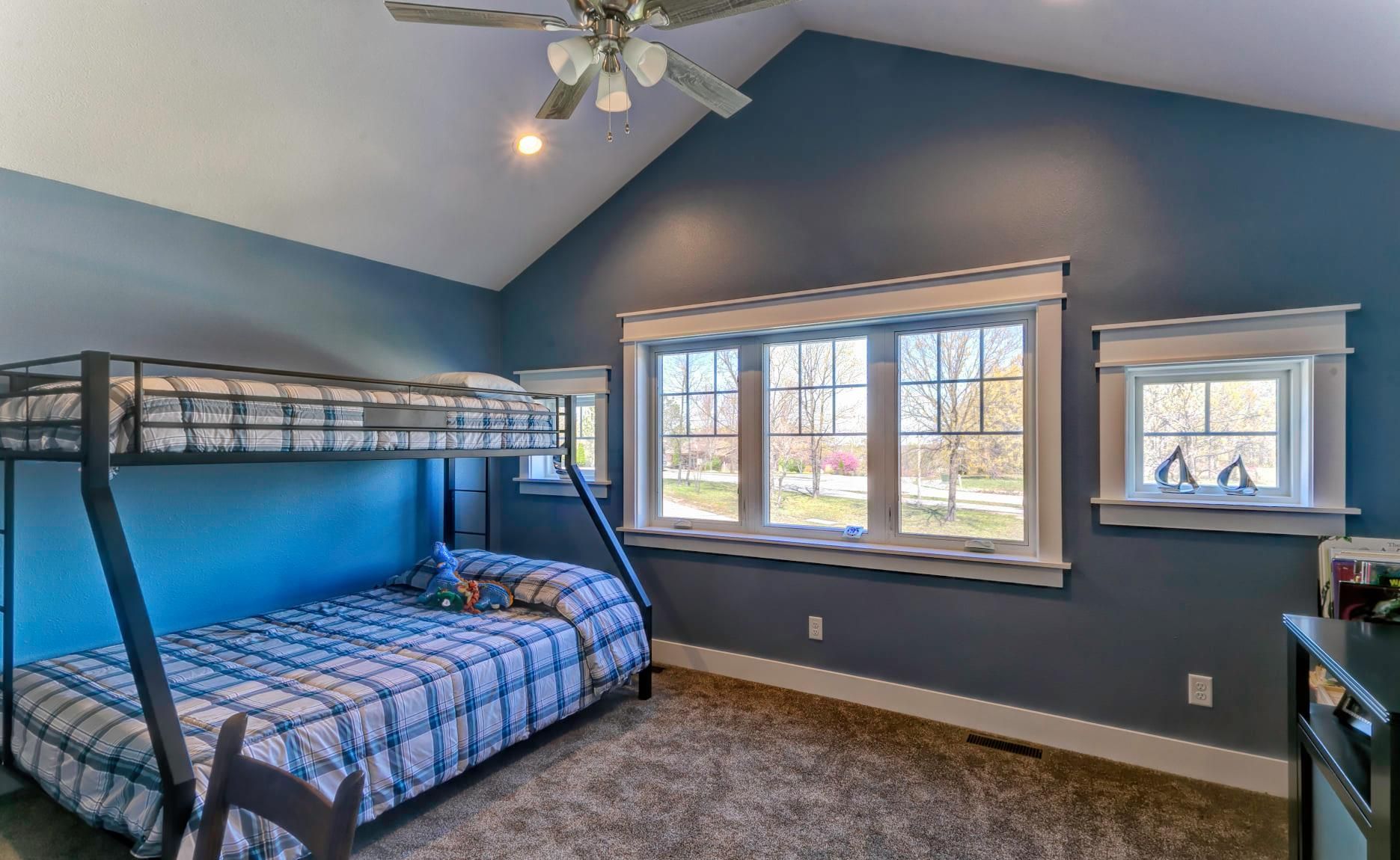 Blue bedroom with bunk bed, carpeted floor, ceiling fan, and windows with blinds.