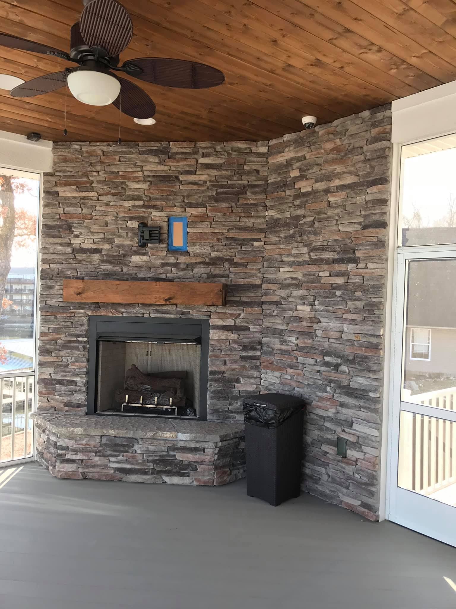 Covered porch with stone fireplace, ceiling fan, and screen door overlooking an outdoor area