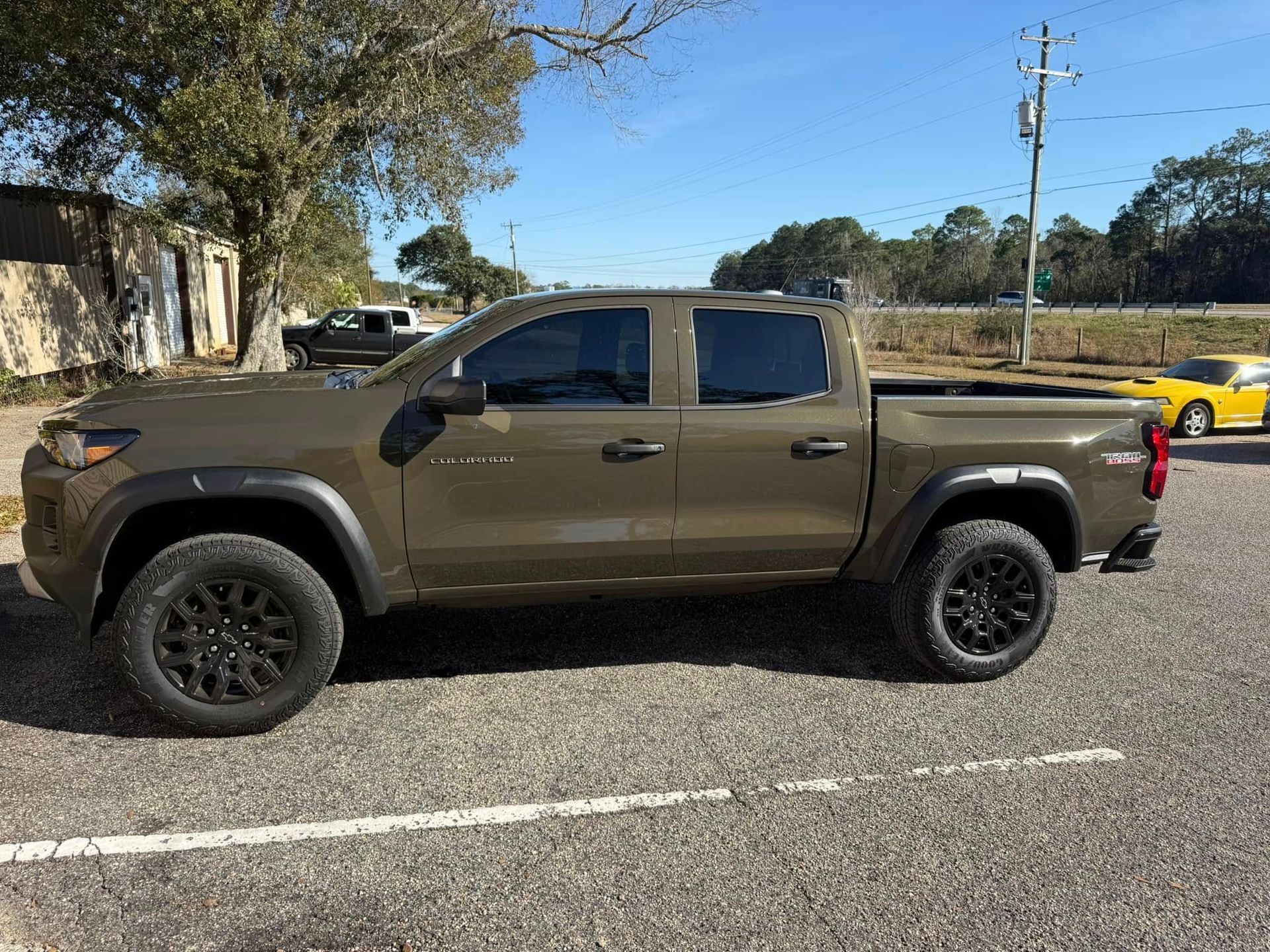 A green truck is parked on the side of the road next to a yellow car.