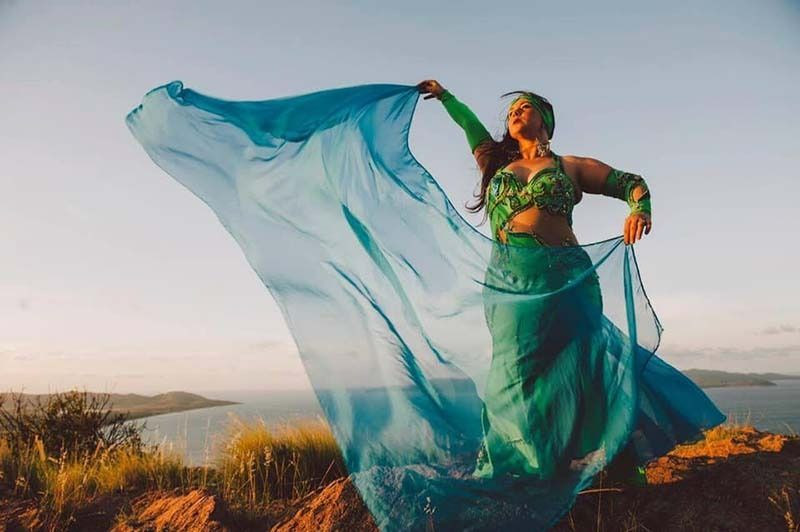 A Belly Dancer Is Standing On Top Of A Rocky Hill Holding A Blue Cloth — Global Dance Collective In West End, QLD