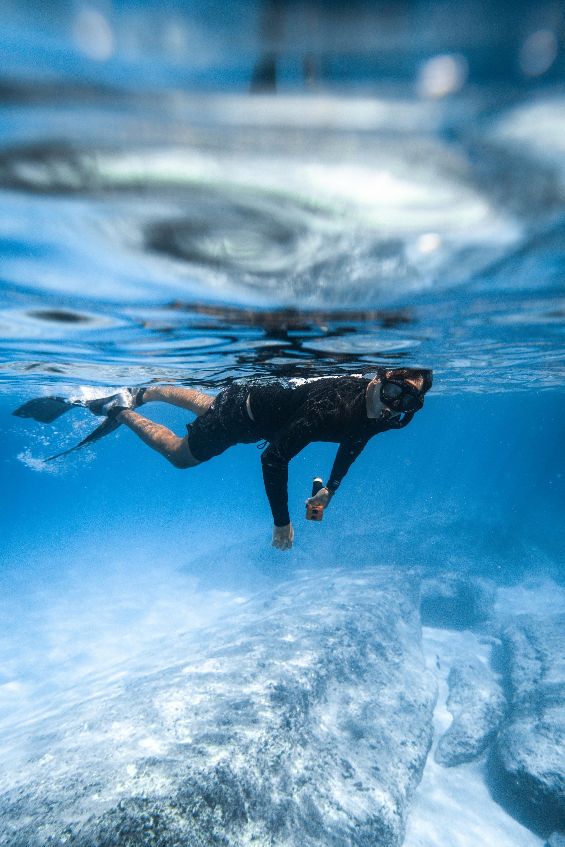 Person snorkeling in clear blue water, wearing a black wetsuit and fins.