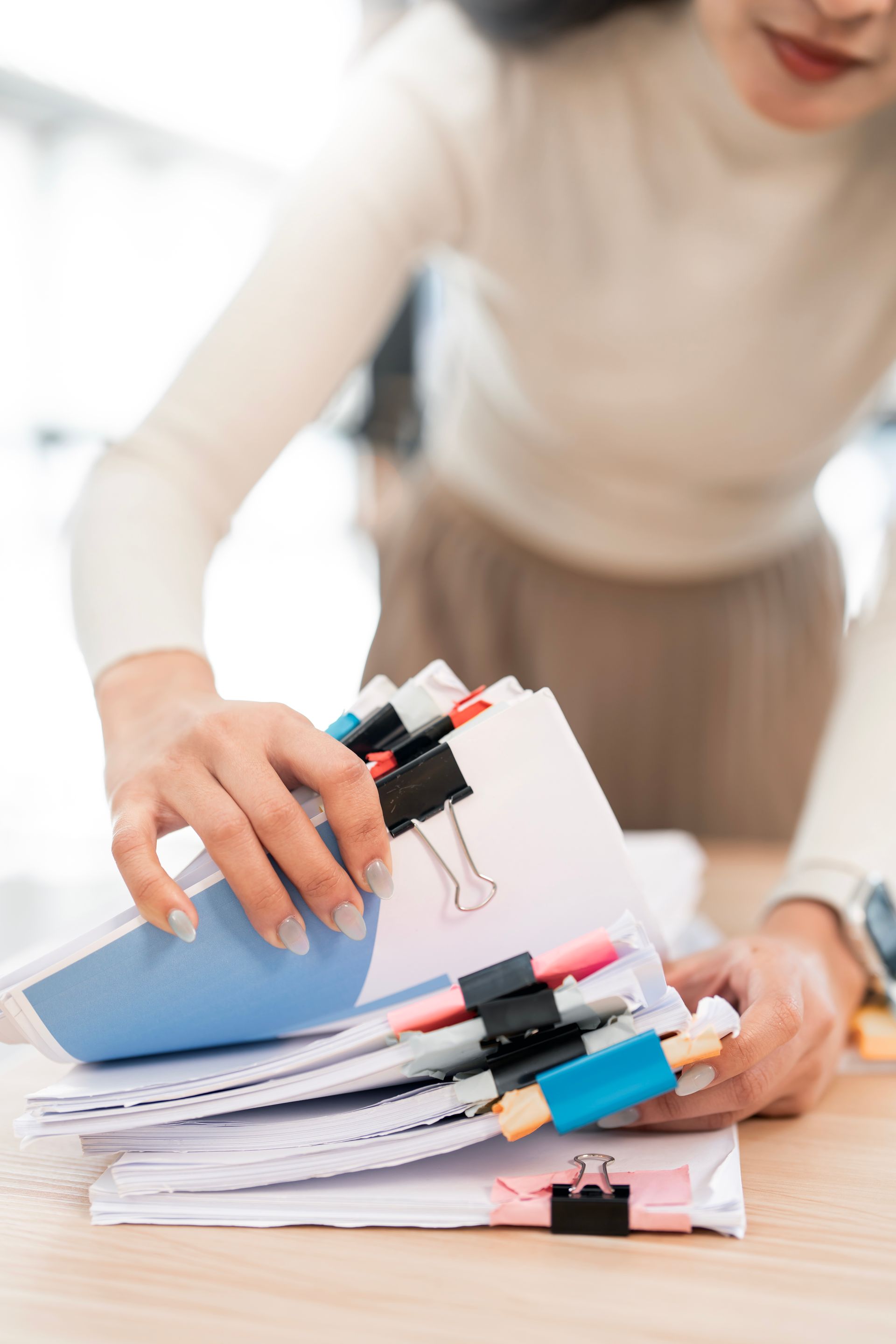 Person organizing a stack of papers with colorful binder clips on a desk