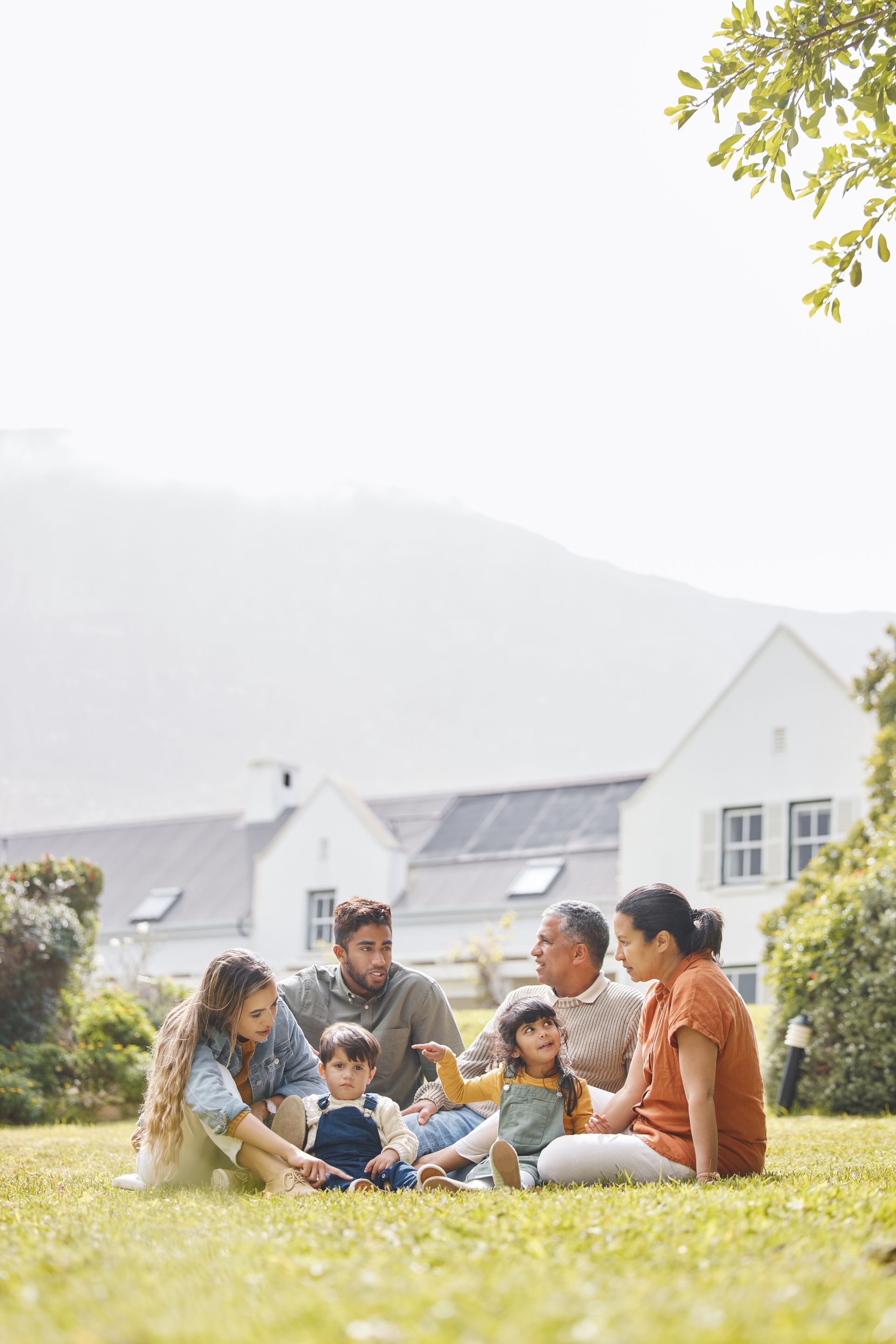 Family sitting on grass in a sunny yard with houses in the background