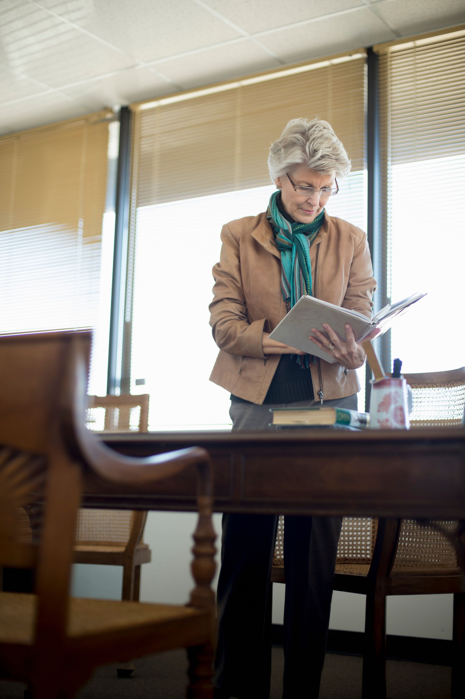 Person reading a book in a sunlit room beside a wooden table and chair