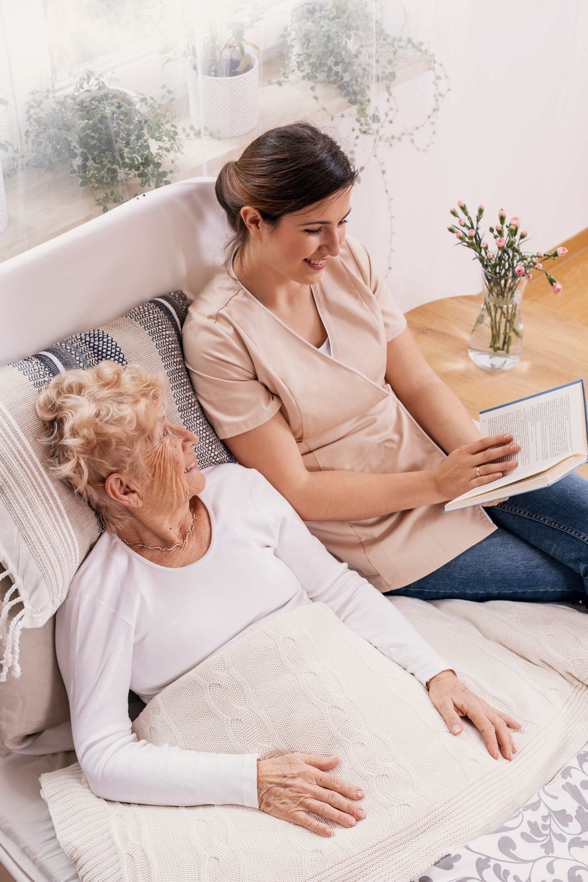 Two people relaxing on a couch, one using a laptop beside a vase of flowers.