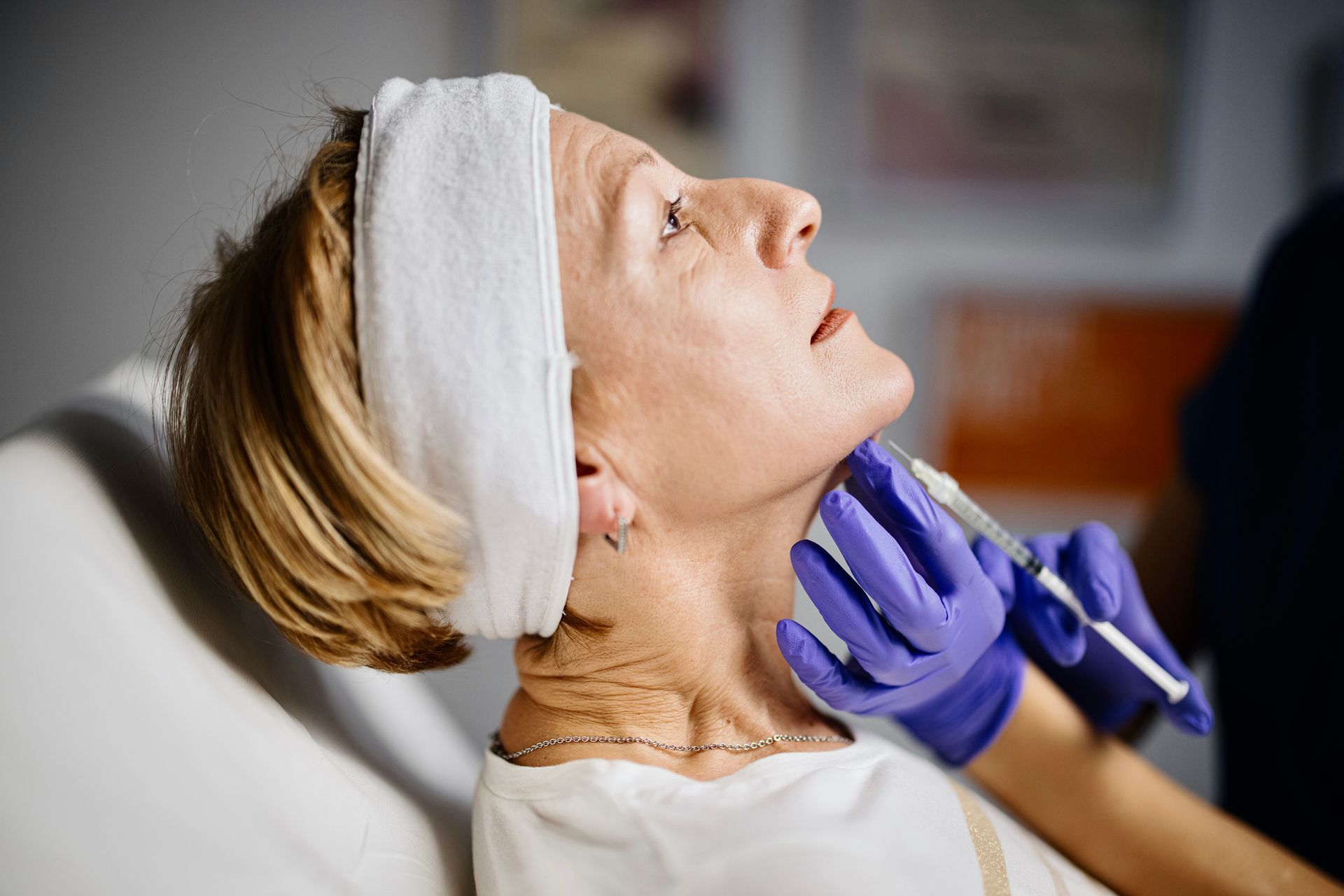 Woman receiving an injection under her chin; wearing a bandage on her head.