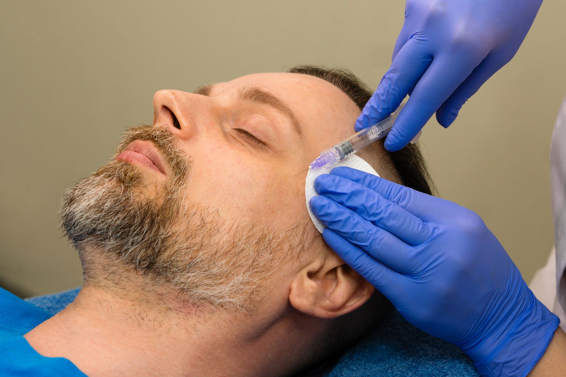 Person receiving an injection in the head. Someone wearing blue gloves administers the injection.