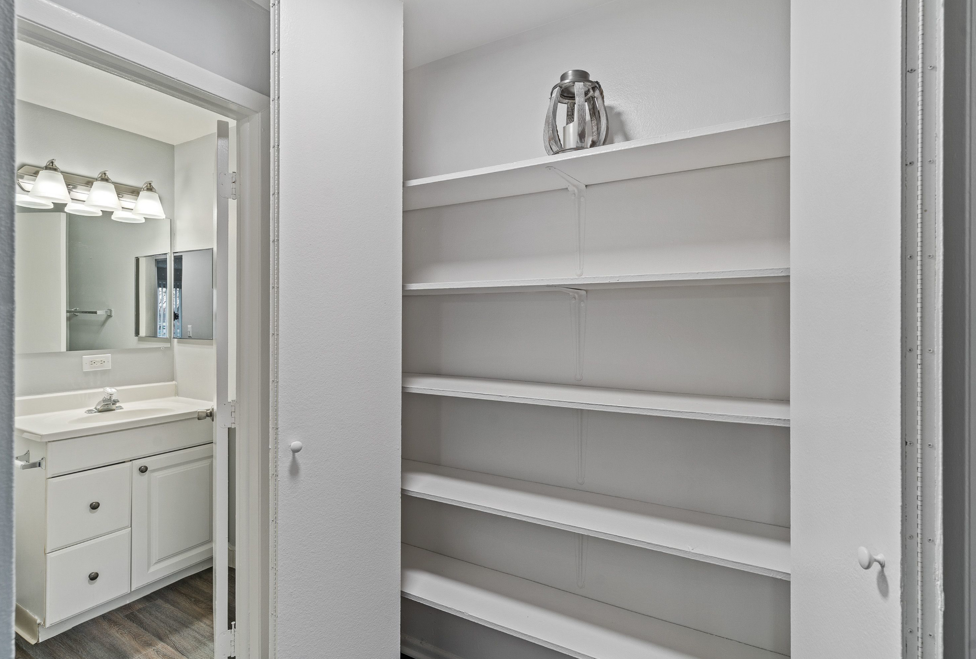 Open built-in white shelving closet beside a bathroom vanity.