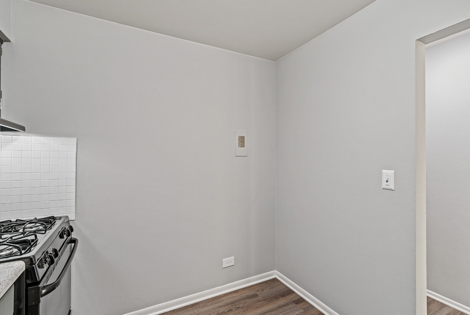 Corner of a small kitchen with a gas stove, gray walls, and wood-look flooring.