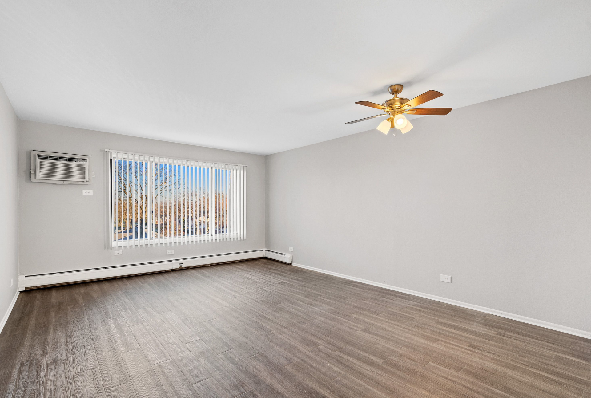 Living room in an apartment with a large window, vertical blinds, and a ceiling fan.