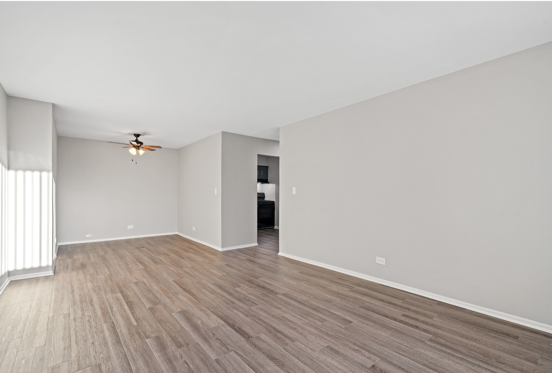 Living room with gray walls, wood-look flooring, ceiling fan, and large window.
