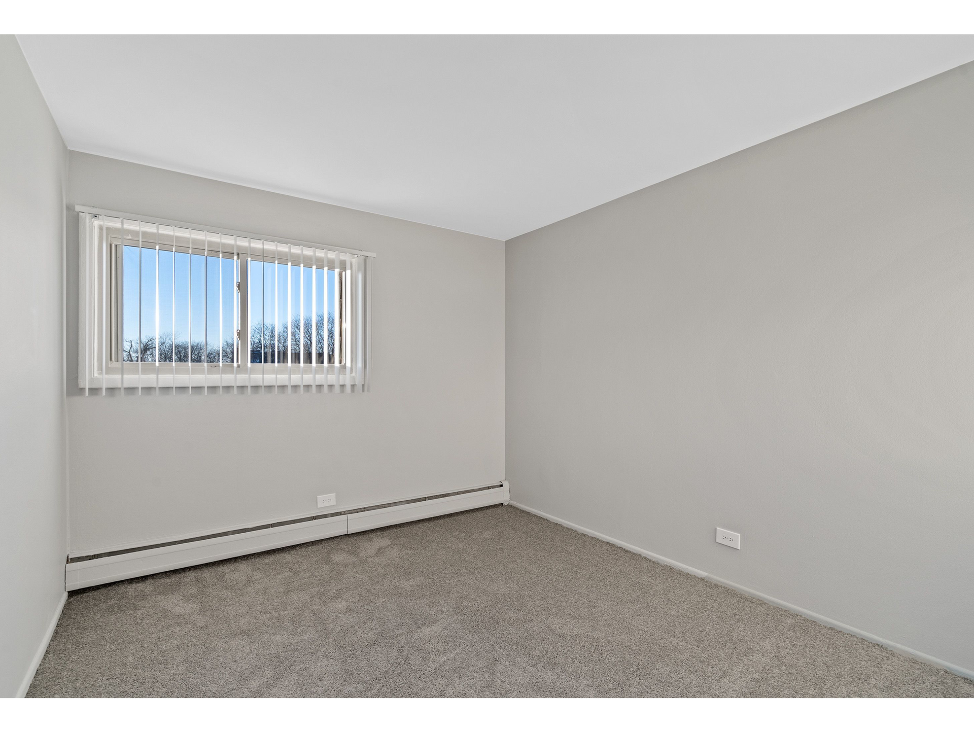 Empty bedroom with a window, vertical blinds, gray walls, and carpet.