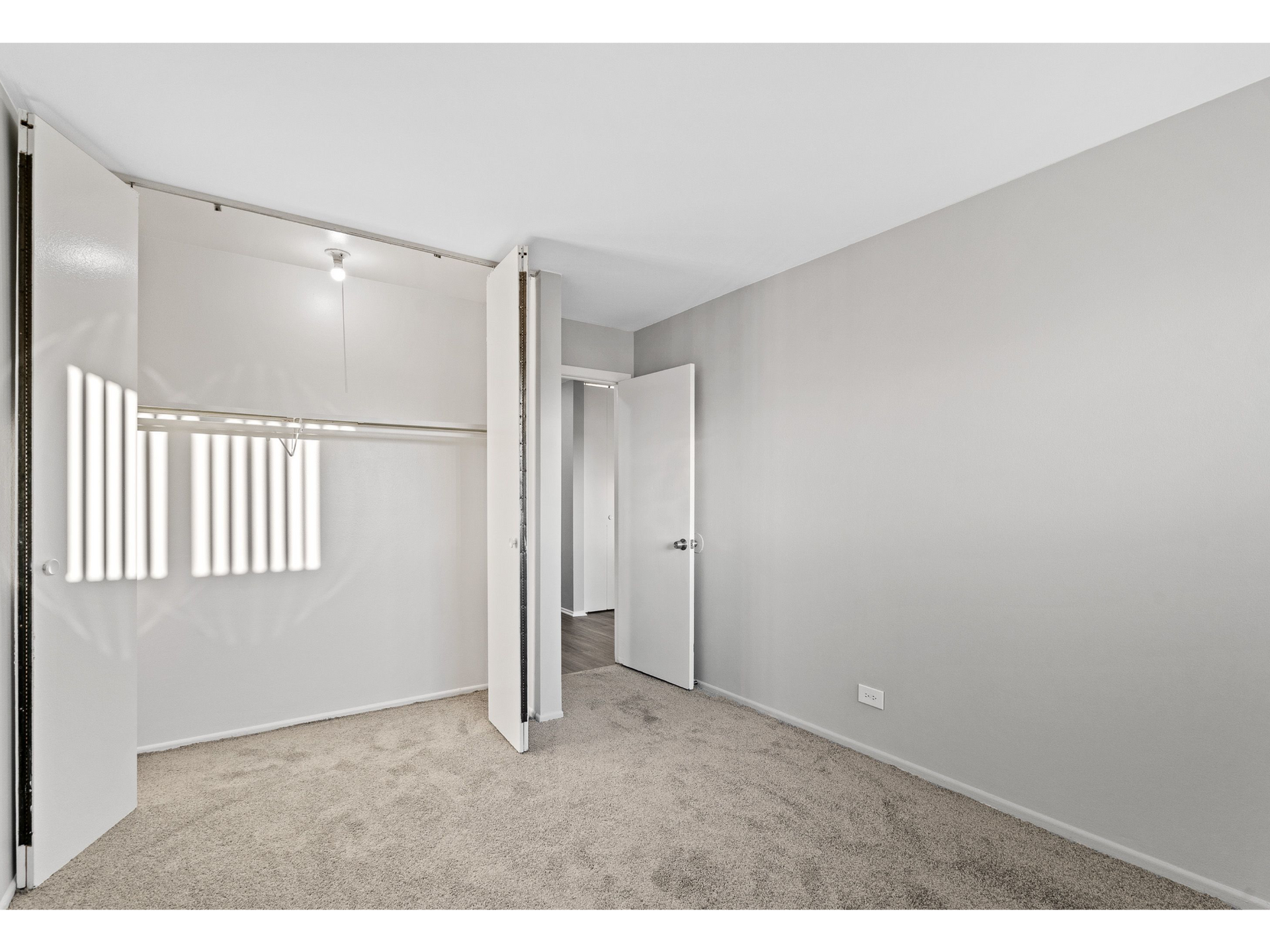 Empty bedroom closet with hanging rod, shelves, and beige carpet.