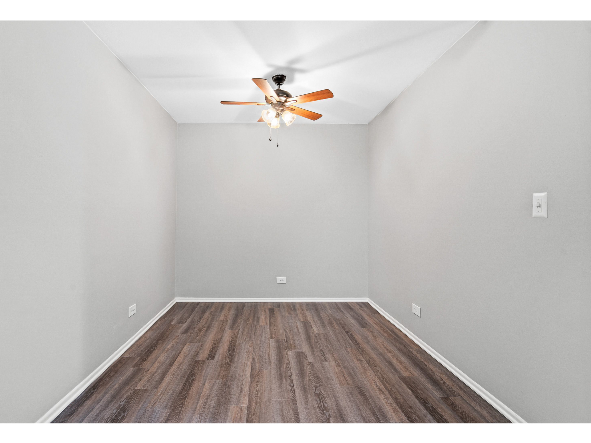 Empty bedroom with gray walls, wood-look laminate flooring, and a ceiling fan.