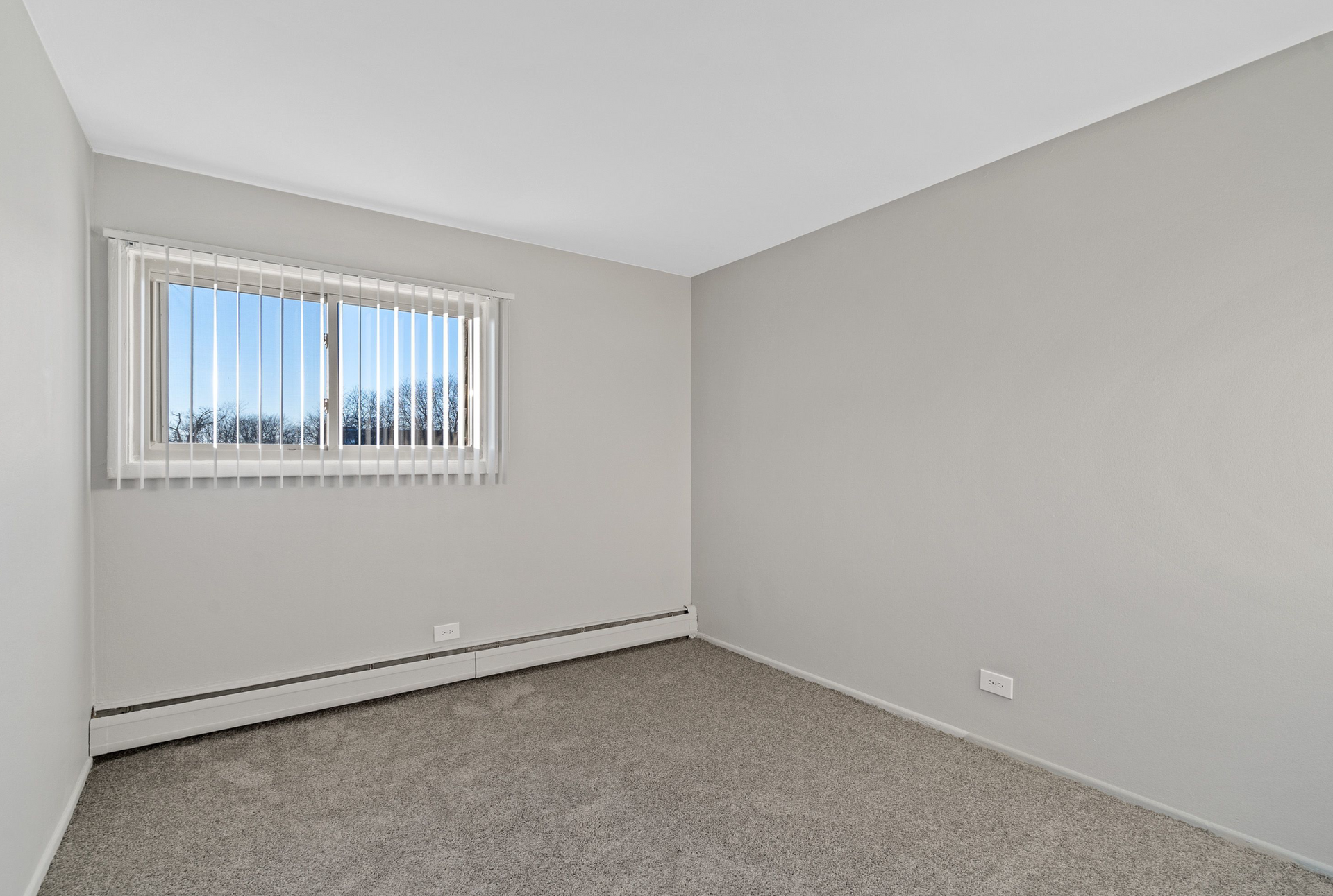 Empty bedroom with a window, vertical blinds, gray walls, and carpet.