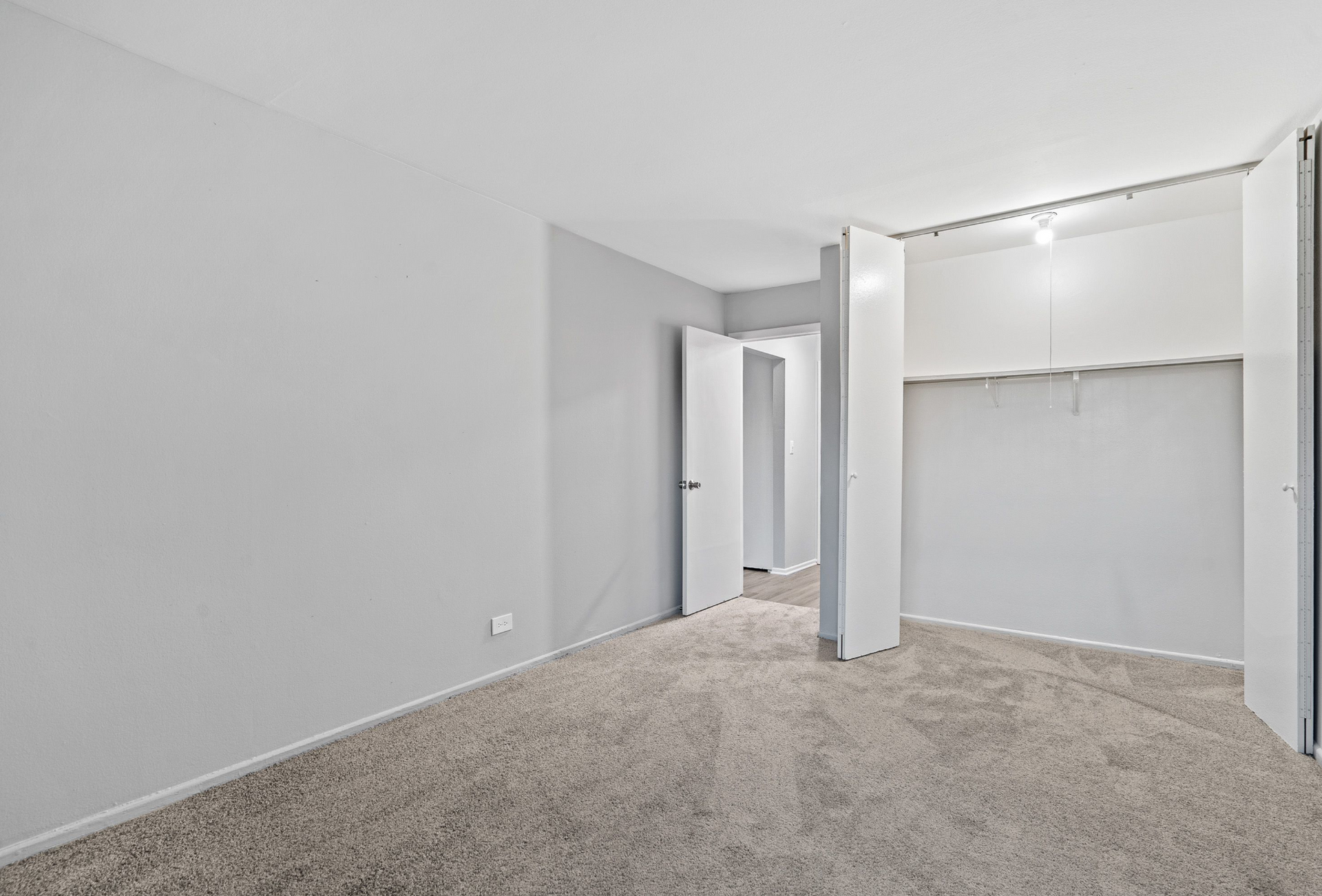 Empty bedroom with light gray walls, beige carpet, and open closet doors.