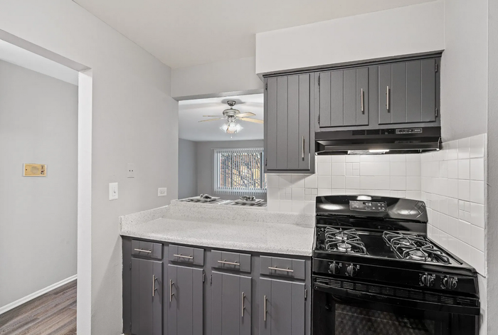 Gray kitchen with dark cabinets, white countertops, and black stove.