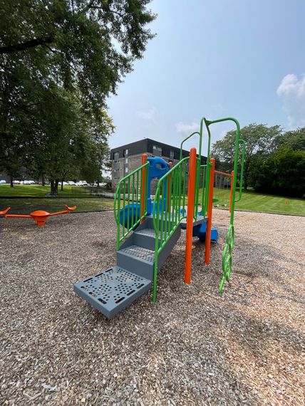 Colorful playground climbing structure on gravel near a grassy field under a blue sky.