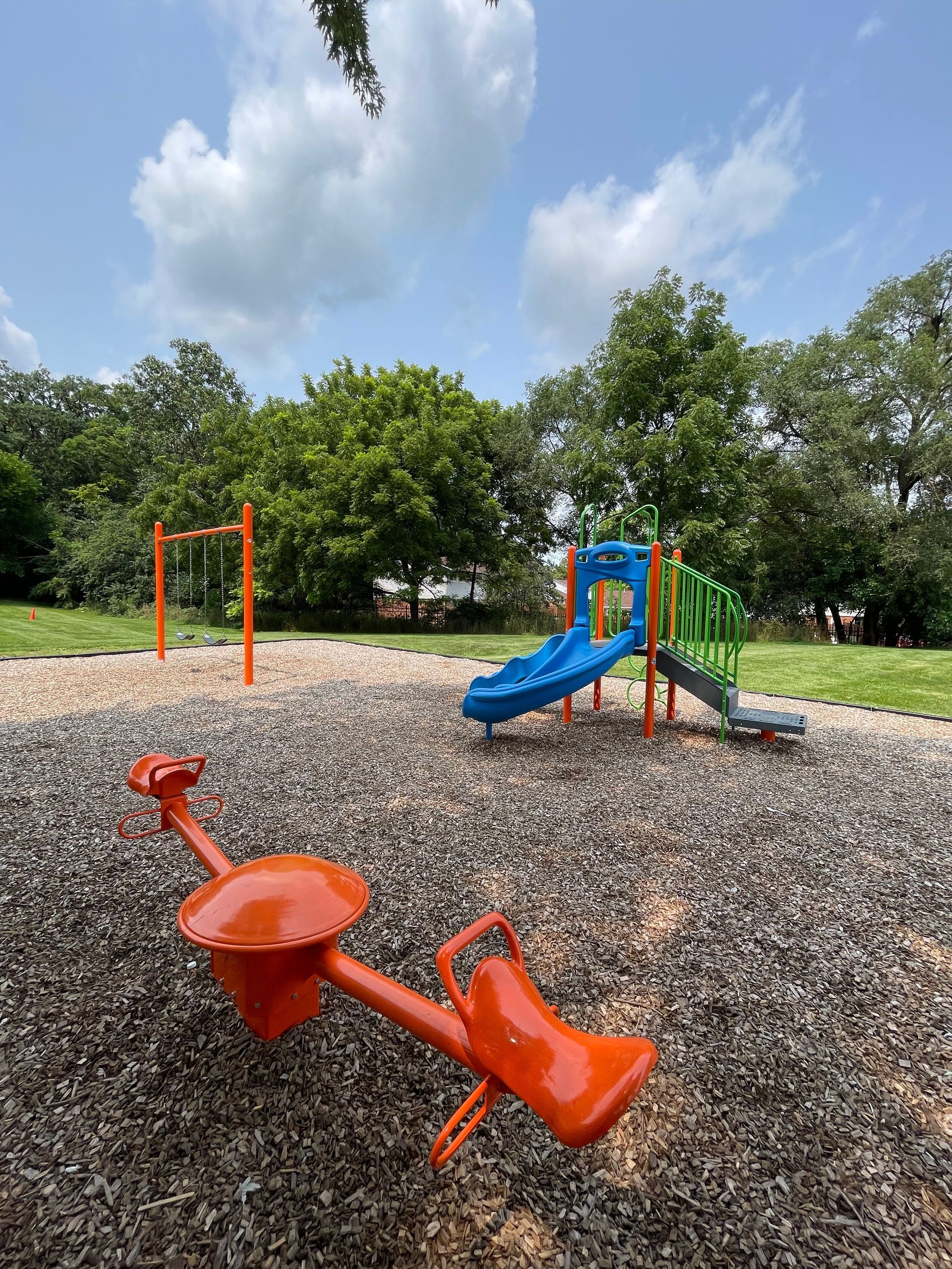 Orange playground spring rider and blue slide on wood chips under a cloudy sky