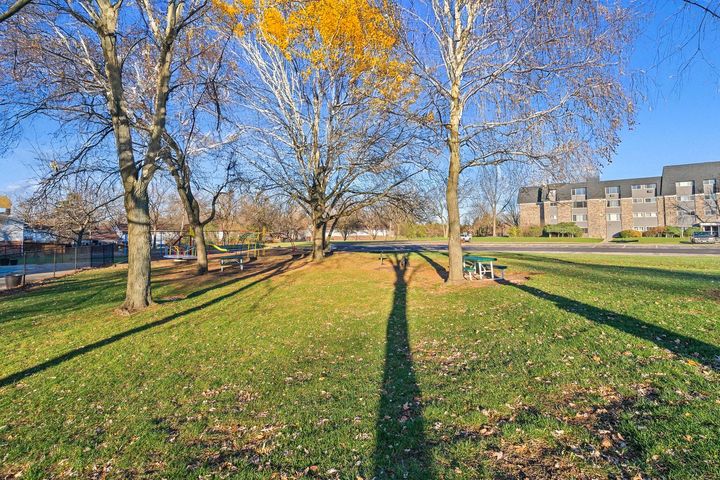Picnic table in a park with bare trees, green grass, and apartment buildings in the background.