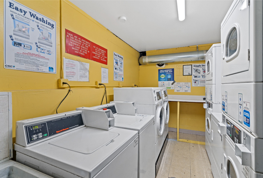 Community laundry room with stacked washing machines and dryers against yellow walls.