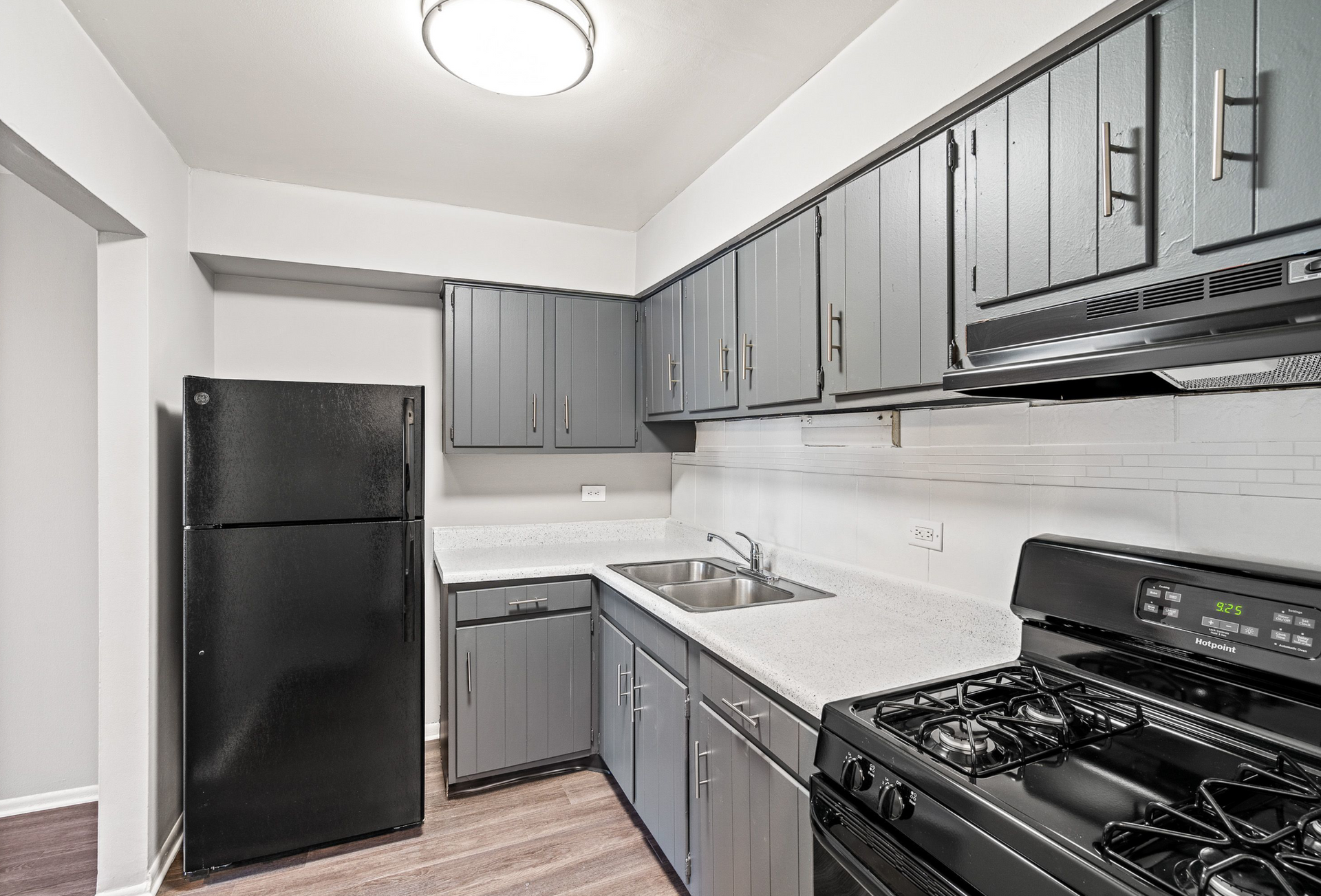 Modern apartment kitchen with gray cabinets, white countertops, sink, fridge, and stove.
