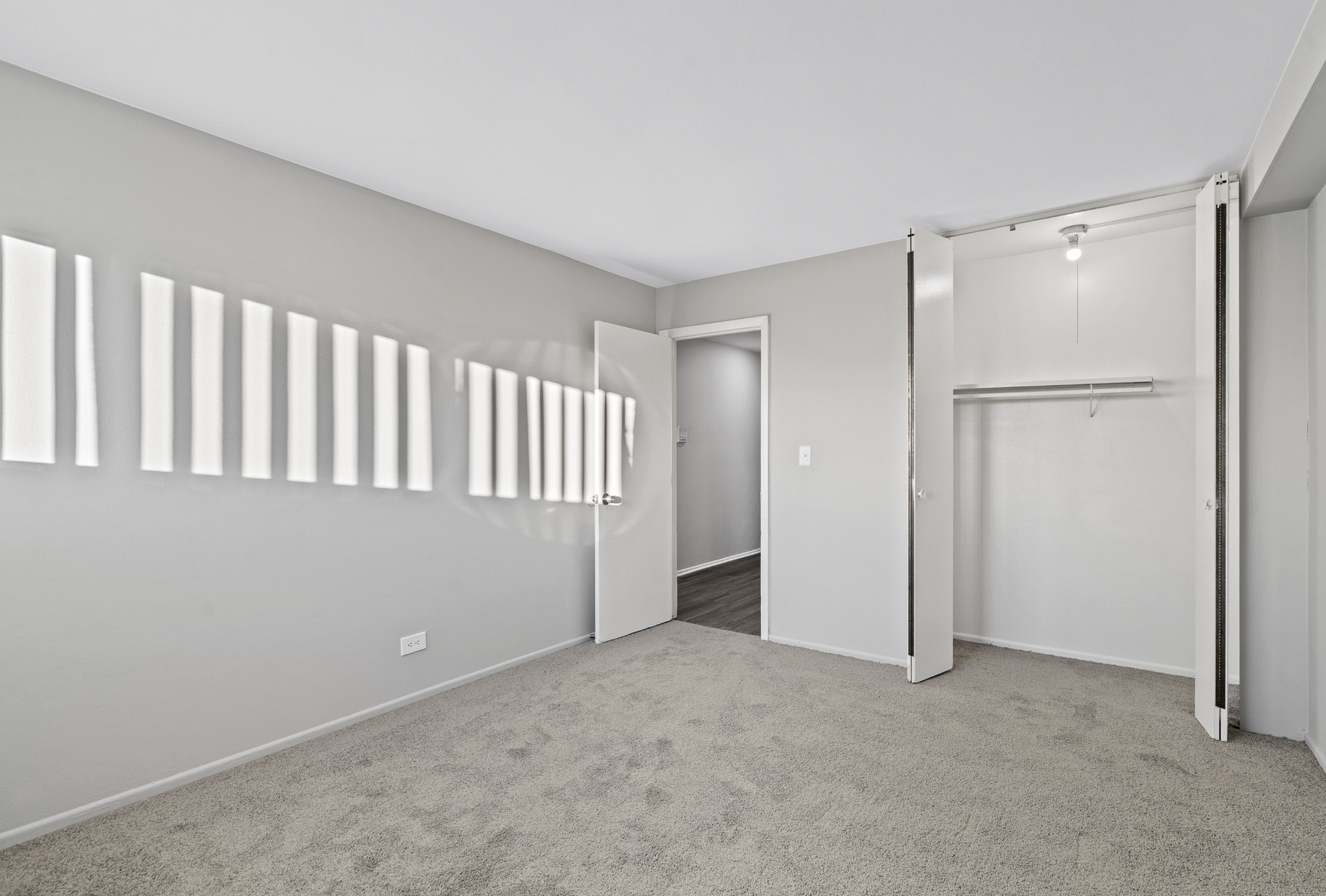 Empty bedroom with gray walls, beige carpet, and an open double-door closet.