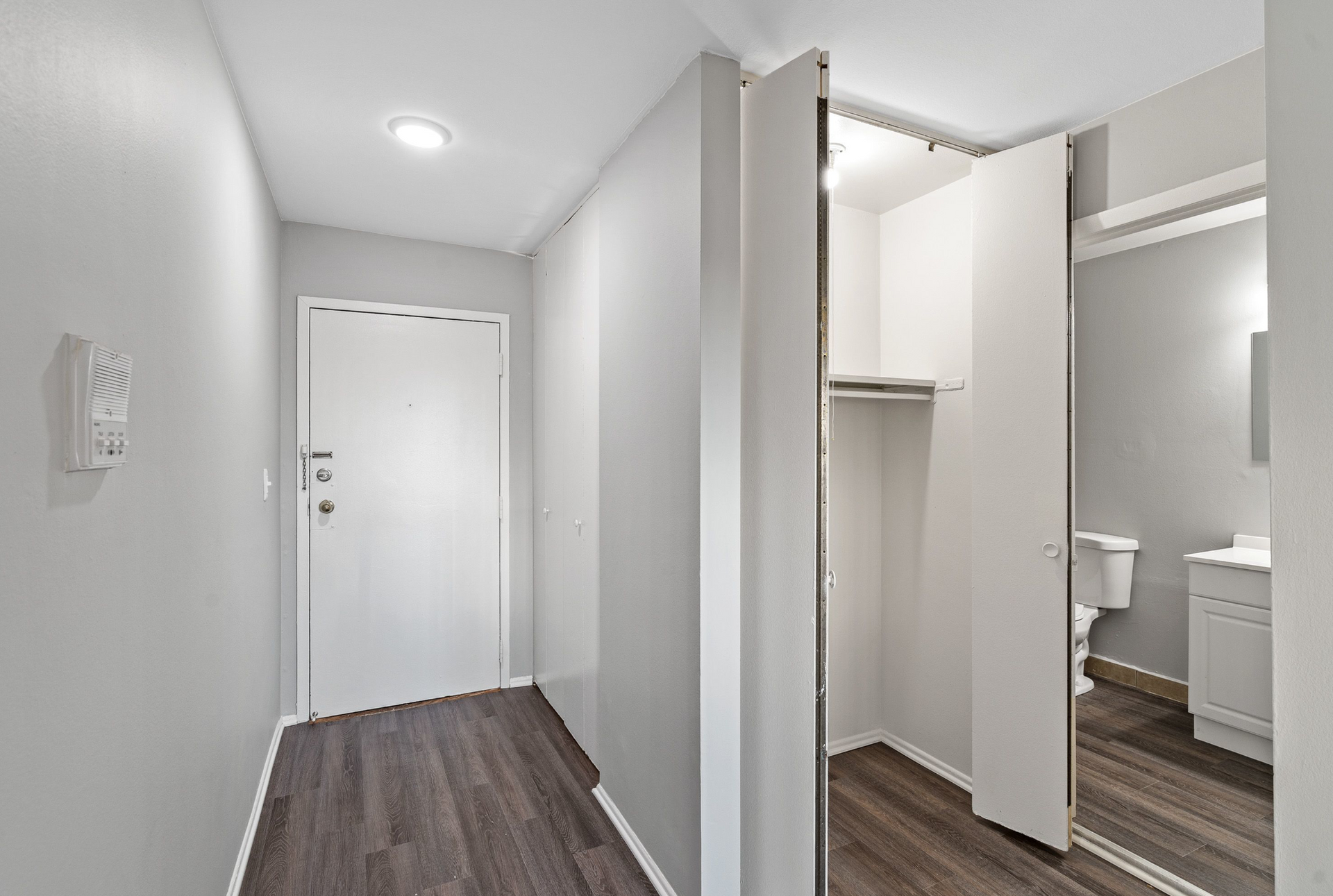 Hallway inside an apartment, showing entry door, open closet, and a bathroom.
