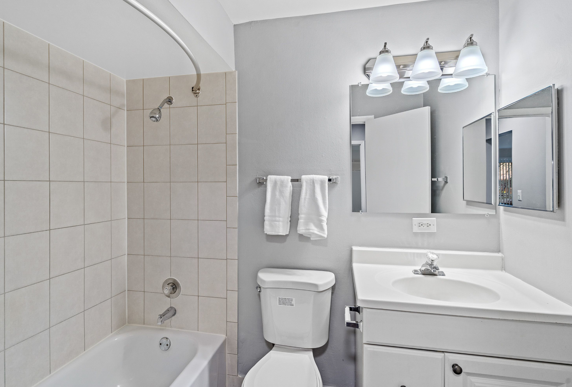 Bathroom in an apartment with tub/shower, tiled walls, toilet, and white vanity with mirror.