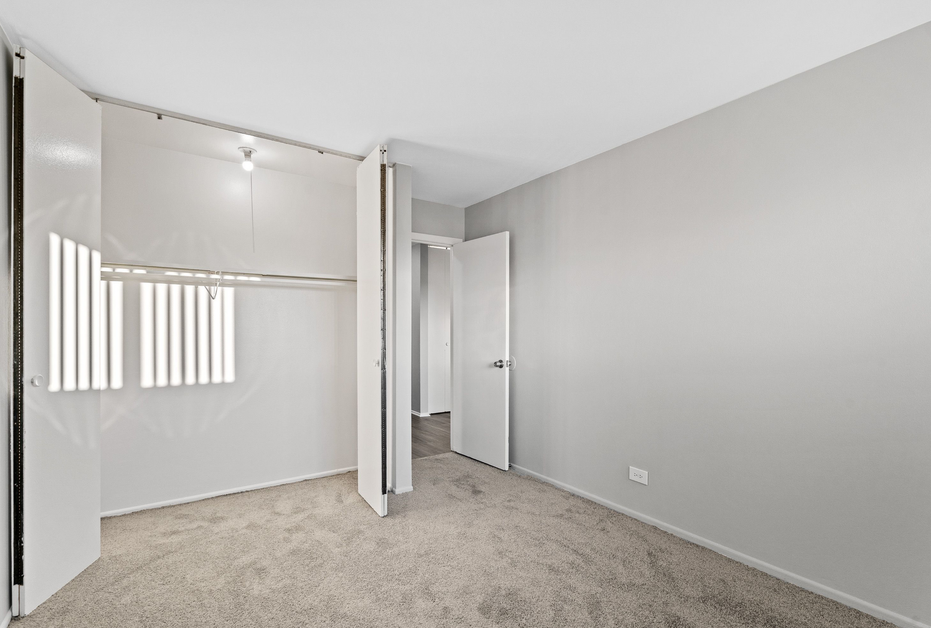 Empty bedroom closet with hanging rod, shelves, and beige carpet.