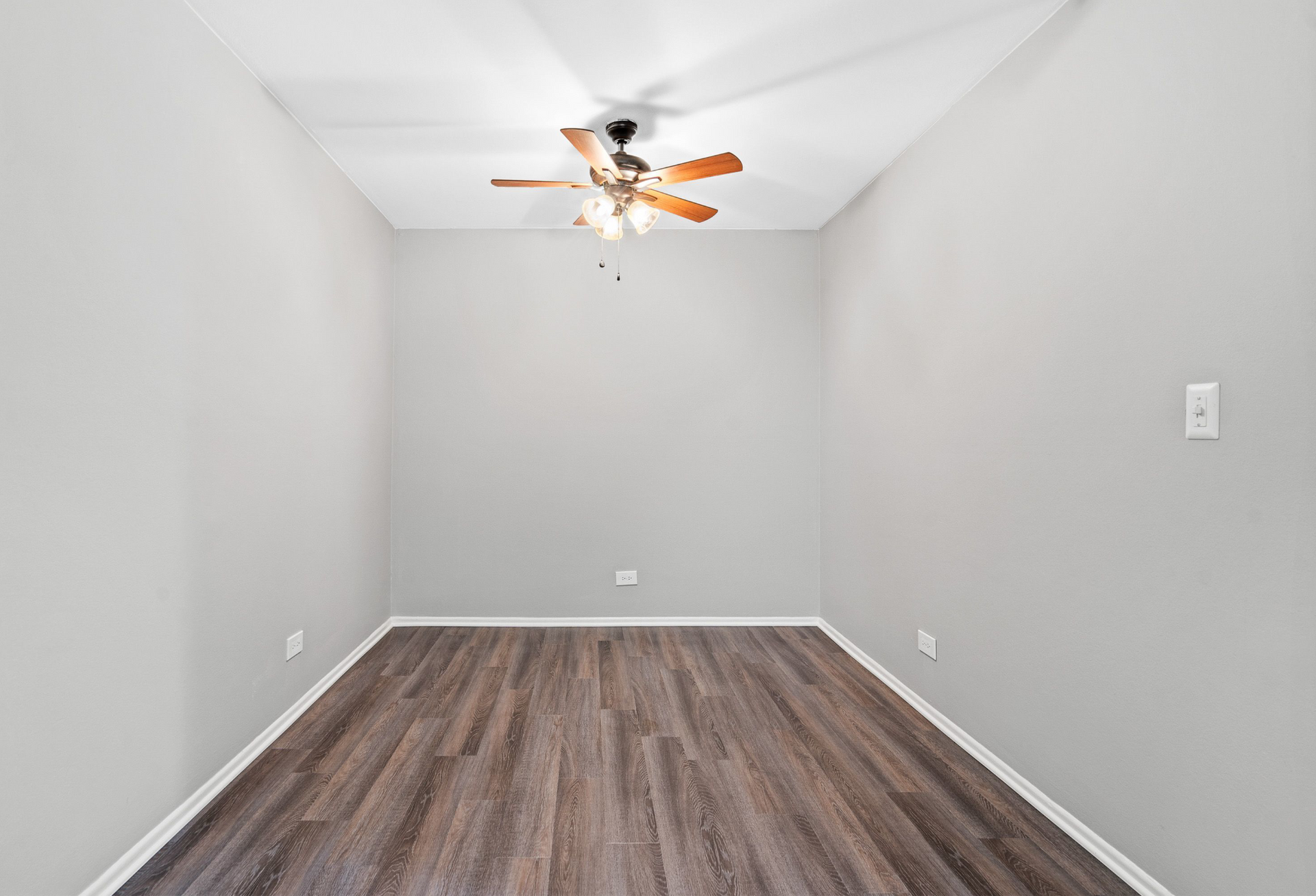 Empty bedroom with gray walls, wood-look laminate flooring, and a ceiling fan.